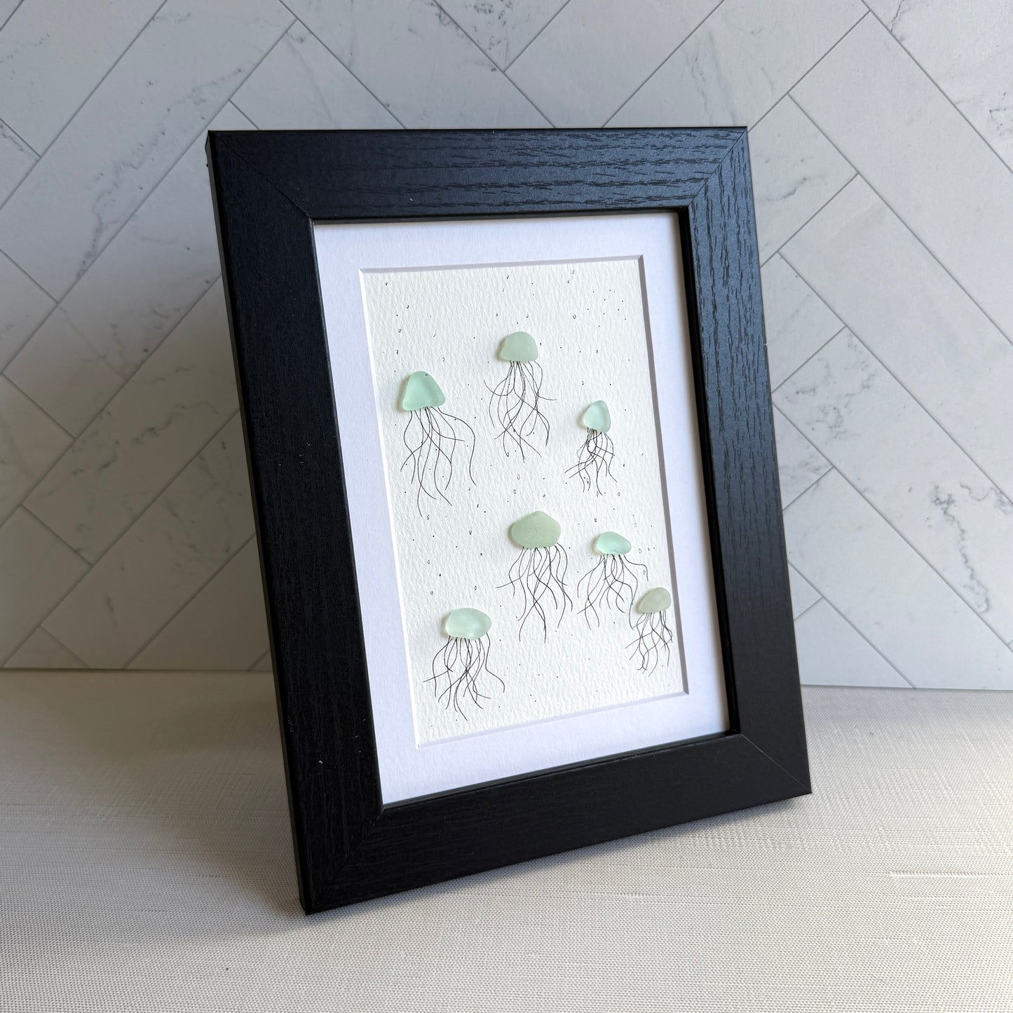 Framed artwork of sea glass jellyfish on a textured wall background