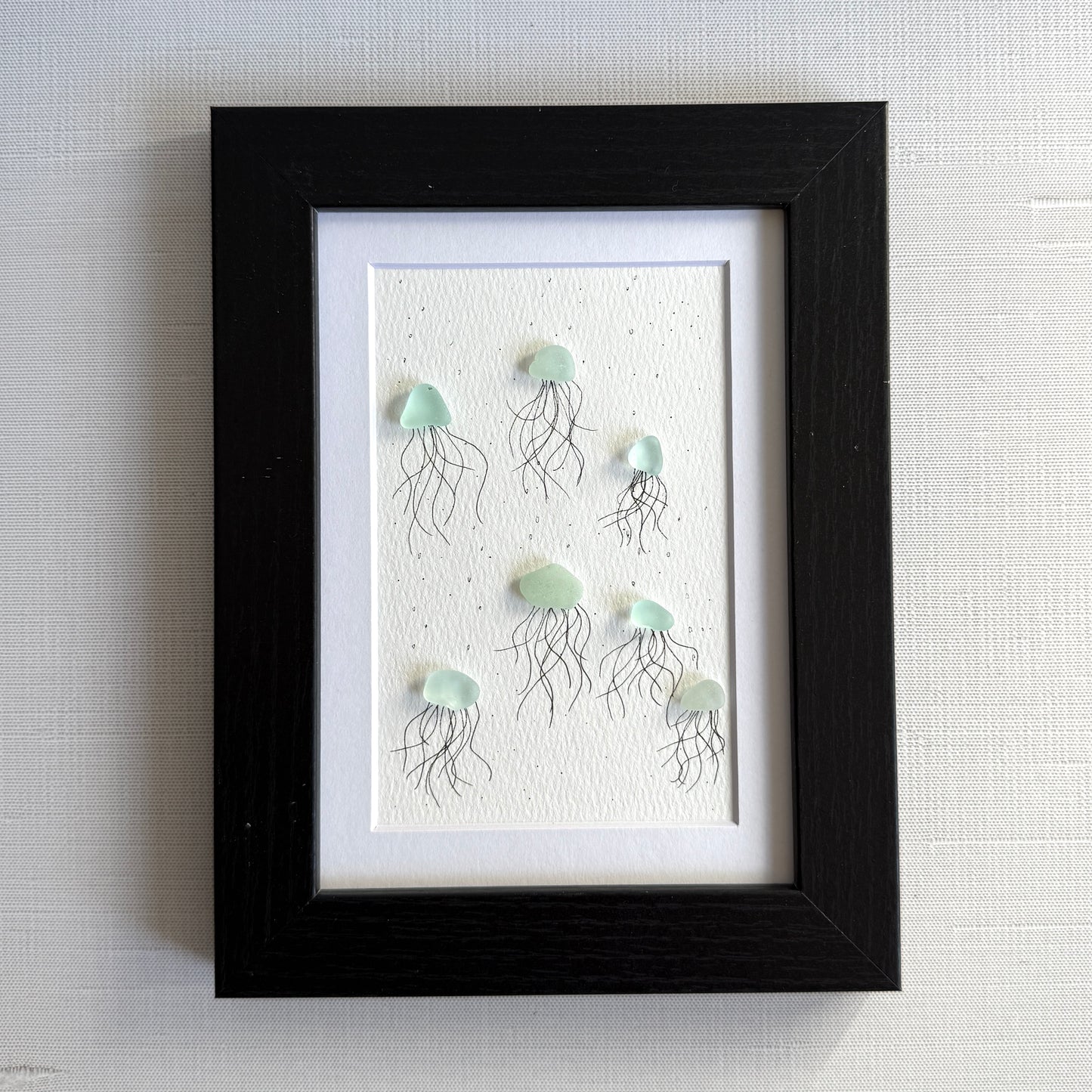Framed artwork of sea glass jellyfish on a textured white background