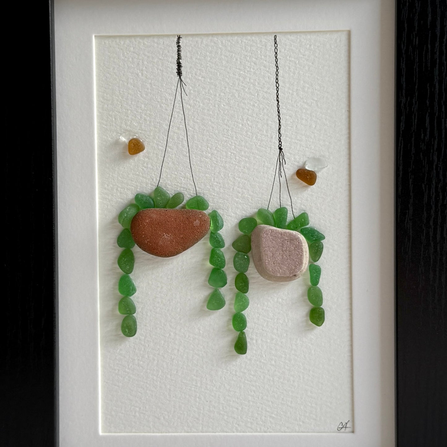 Decorative sea glass wall art of hanging plant pots with green sea glass on a textured white background.
