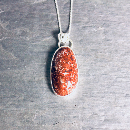May include: A silver chain necklace with a red and white oval pendant. The pendant is made of a natural stone with a unique pattern.