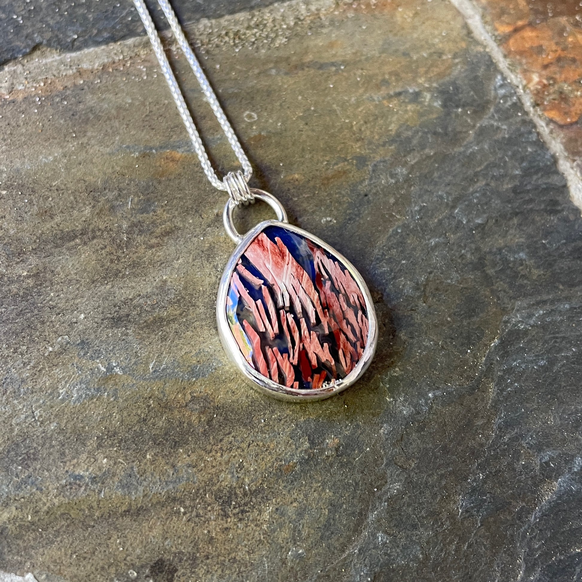 A handmade teardrop shaped doublet cabochon of howardite (rattlesnake jasper) and lapis lazuli set in a fine and sterling silver bezel setting on a sterling silver chain. 