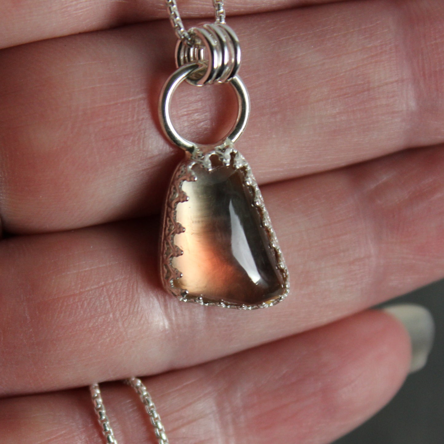 This is an approximately 12mm x 18mm Oregon sunstone with red and shiller throughout.  It has a fancy sterling silver bezel setting. 