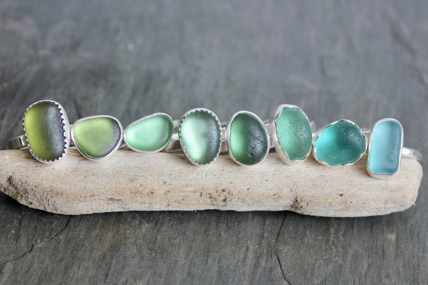 Set of sea glass rings on a piece of driftwood with a dark stone background
