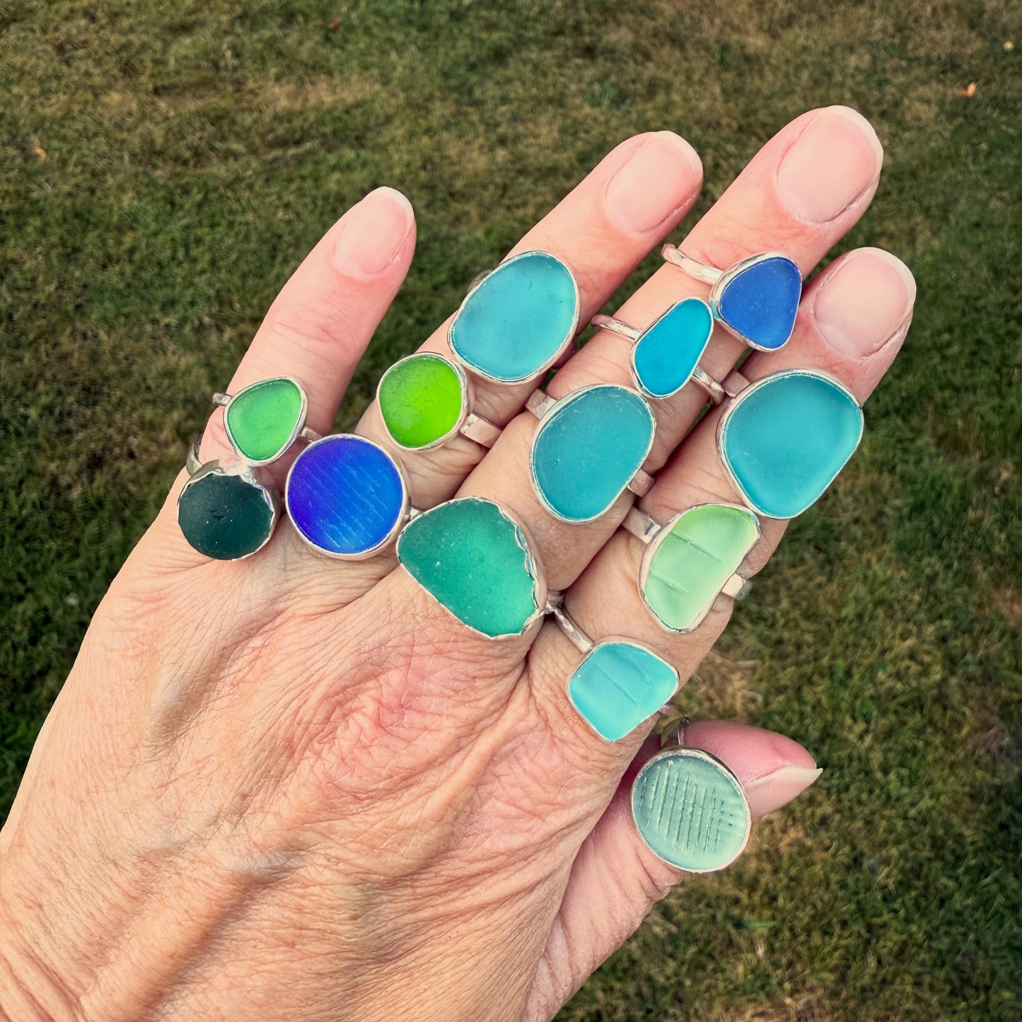 Hand wearing multiple colorful rings on a grassy background