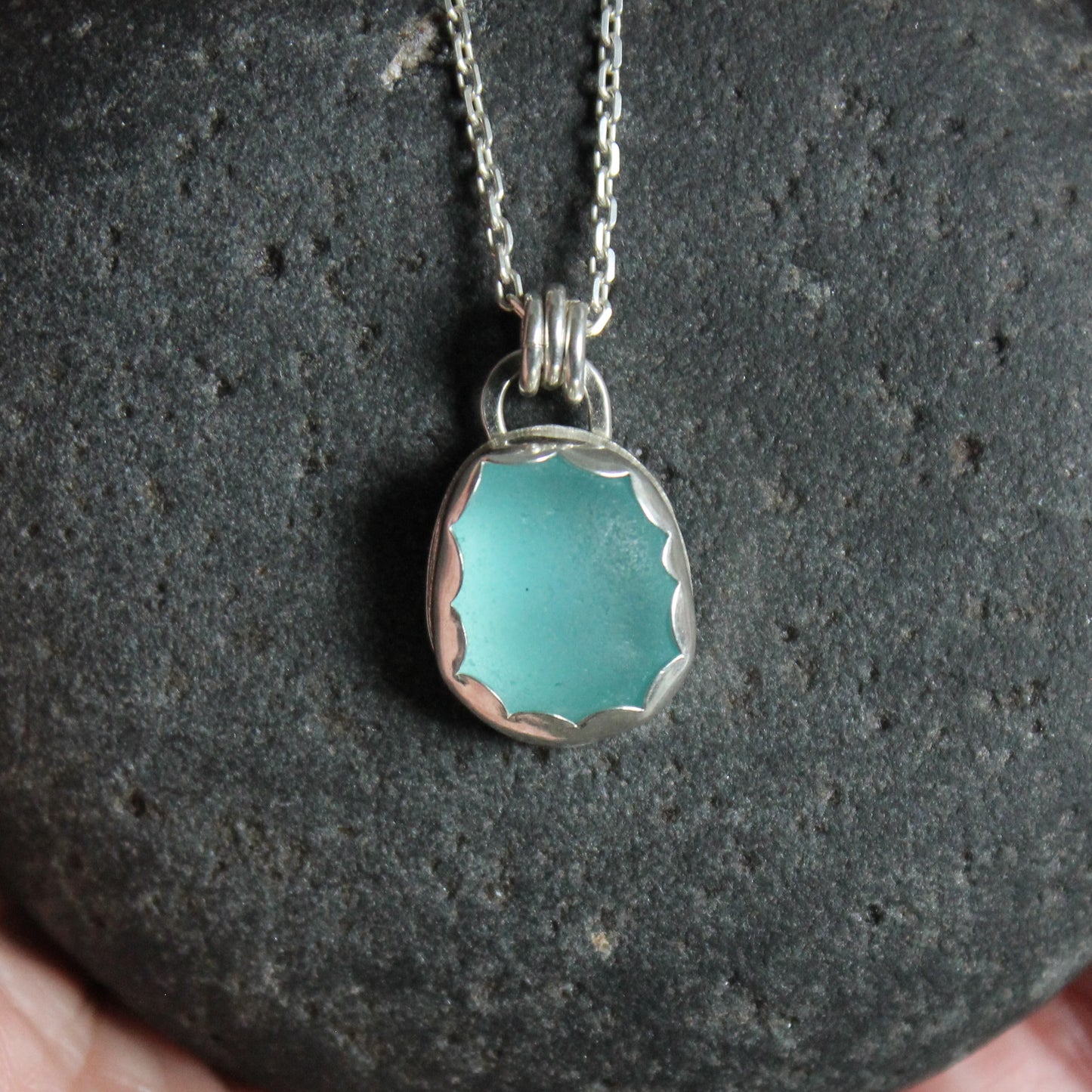 A small piece of aqua blue sea glass set in a fine and sterling silver scalloped bezel setting on a sterling silver chain. 