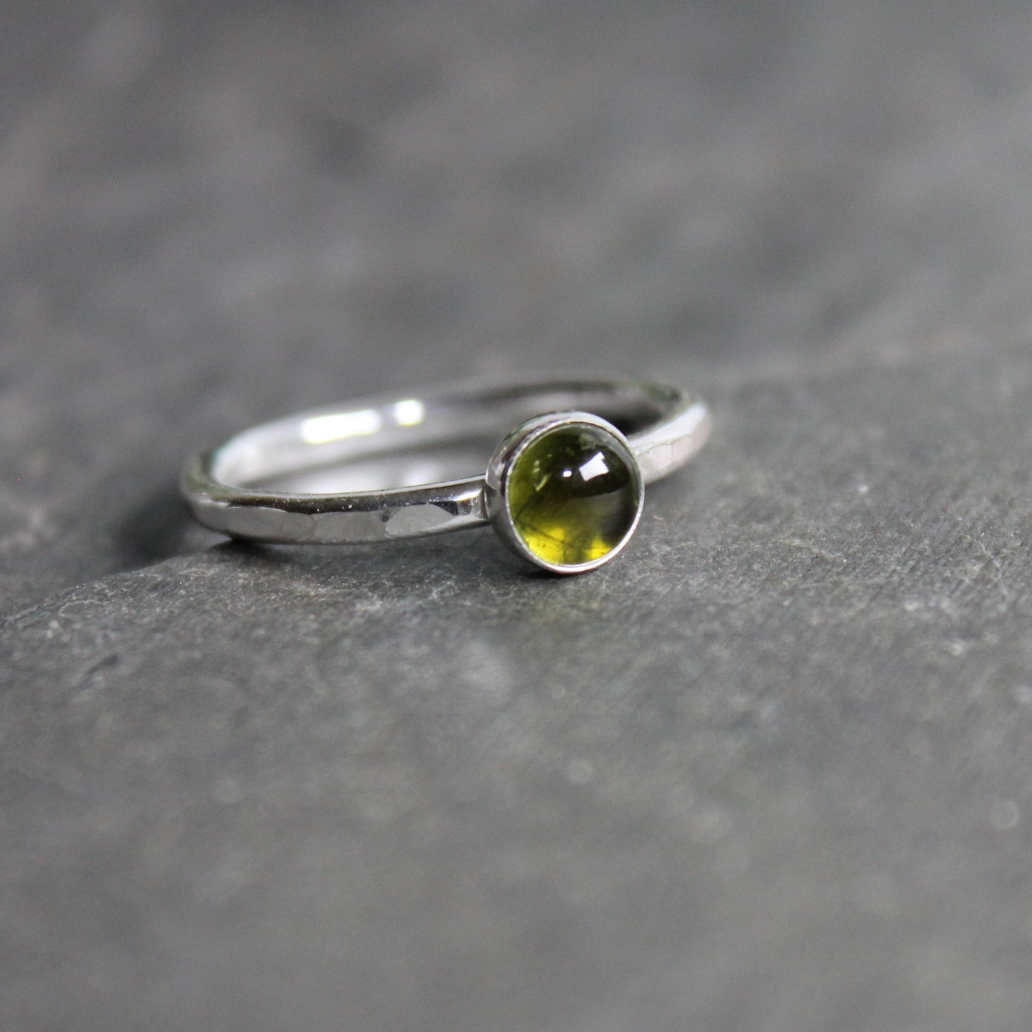 A Round 6mm green tourmaline gemstone set in a sterling silver bezel setting on a sturdy hammered band. 