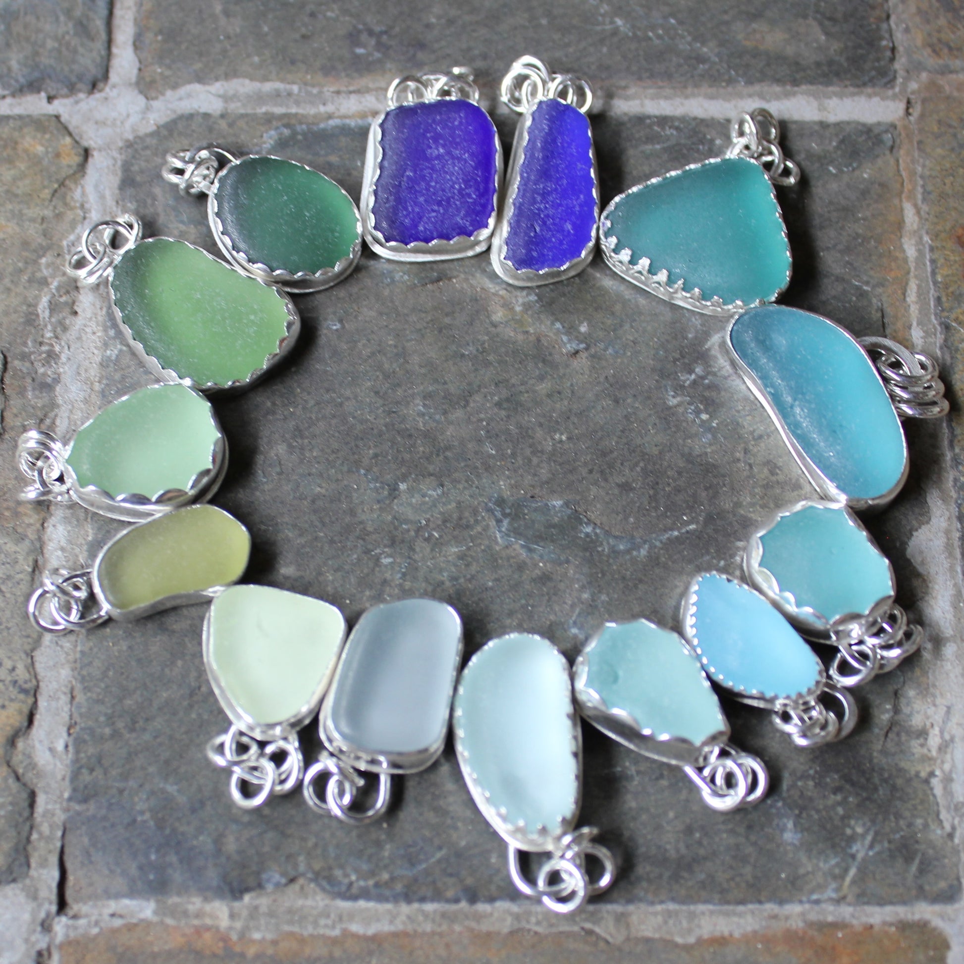 A circle of handmade sterling silver sea glass pendants in shades of blues and greens