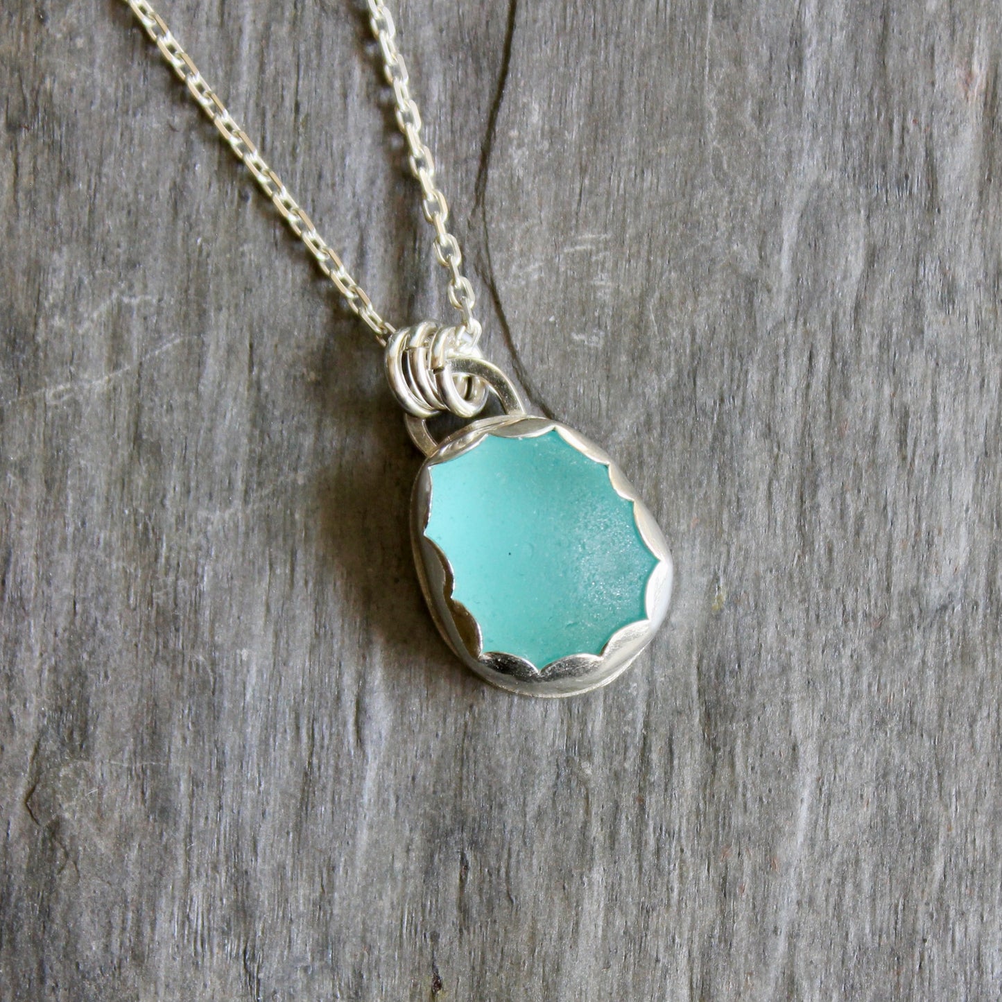 This is a small piece of aqua blue sea glass set in a fine & sterling silver scalloped bezel setting on an 18 inch chain. 