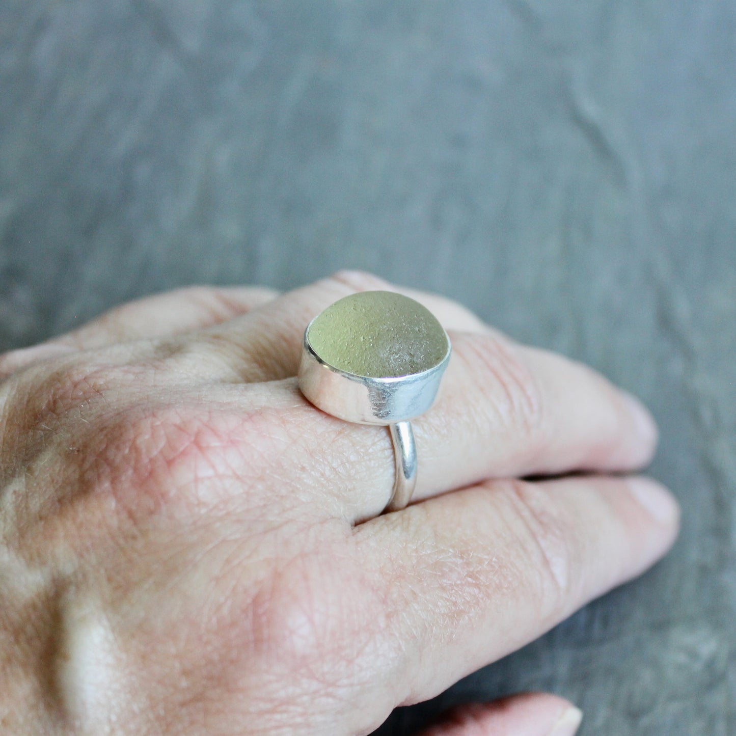 Silver ring with a Champagne Sea Glass on a hand against a gray background