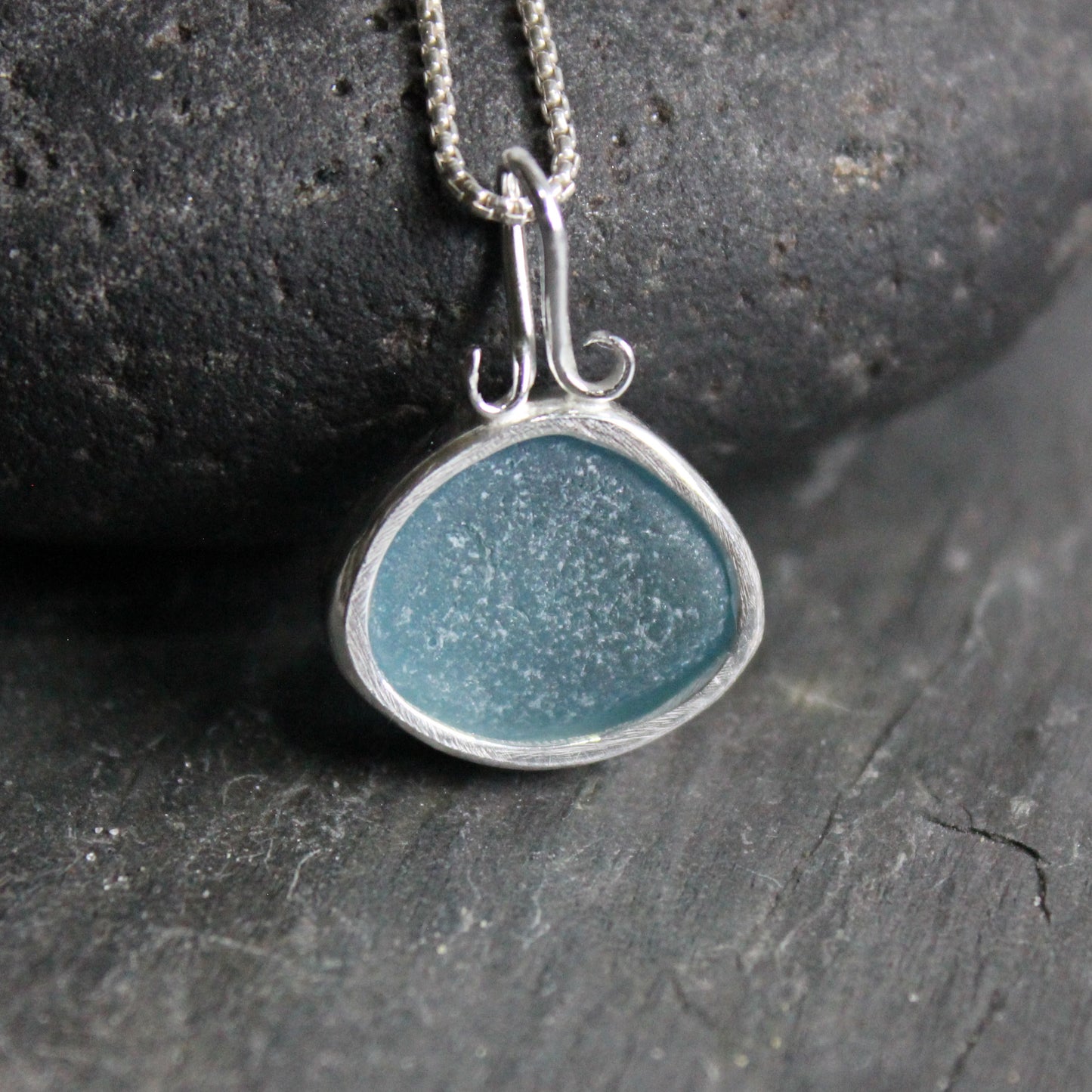This is a large piece of teal sea glass set in a fine and sterling silver scalloped bezel setting with a fancy bail. back side view