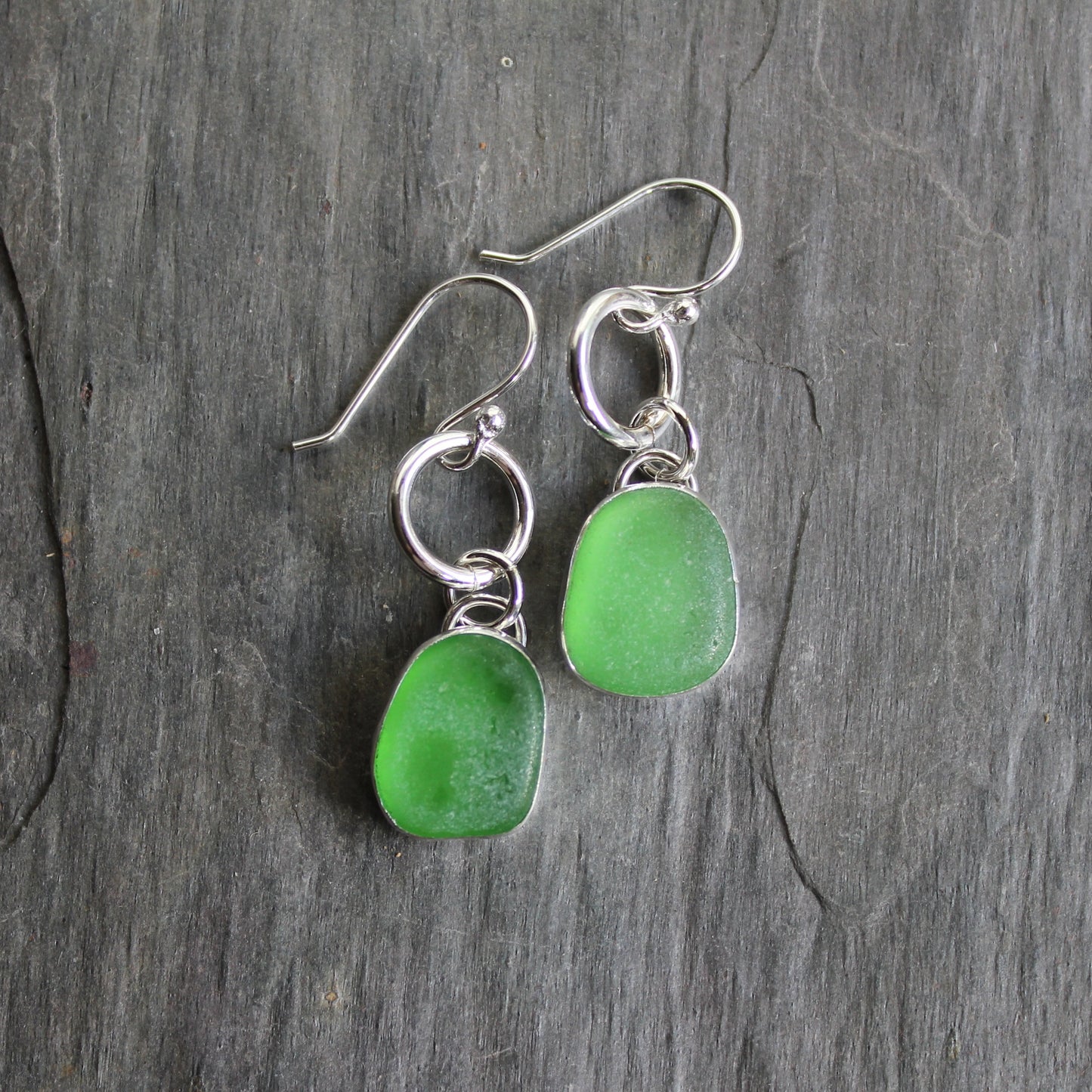 This is a pair of dangly bright green sea glass earrings with approximately 1/2" sea glass set in fine and sterling silver bezel settings and attached to a ring & ear wires. Accent Yourself specializes in sterling silver jewelry handmade by Barb Macy and Will Macy in Corvallis, OR including sea glass jewelry, Oregon sunstones, sterling silver earrings, and jewelry made with gemstones found in the Pacific Northwest.