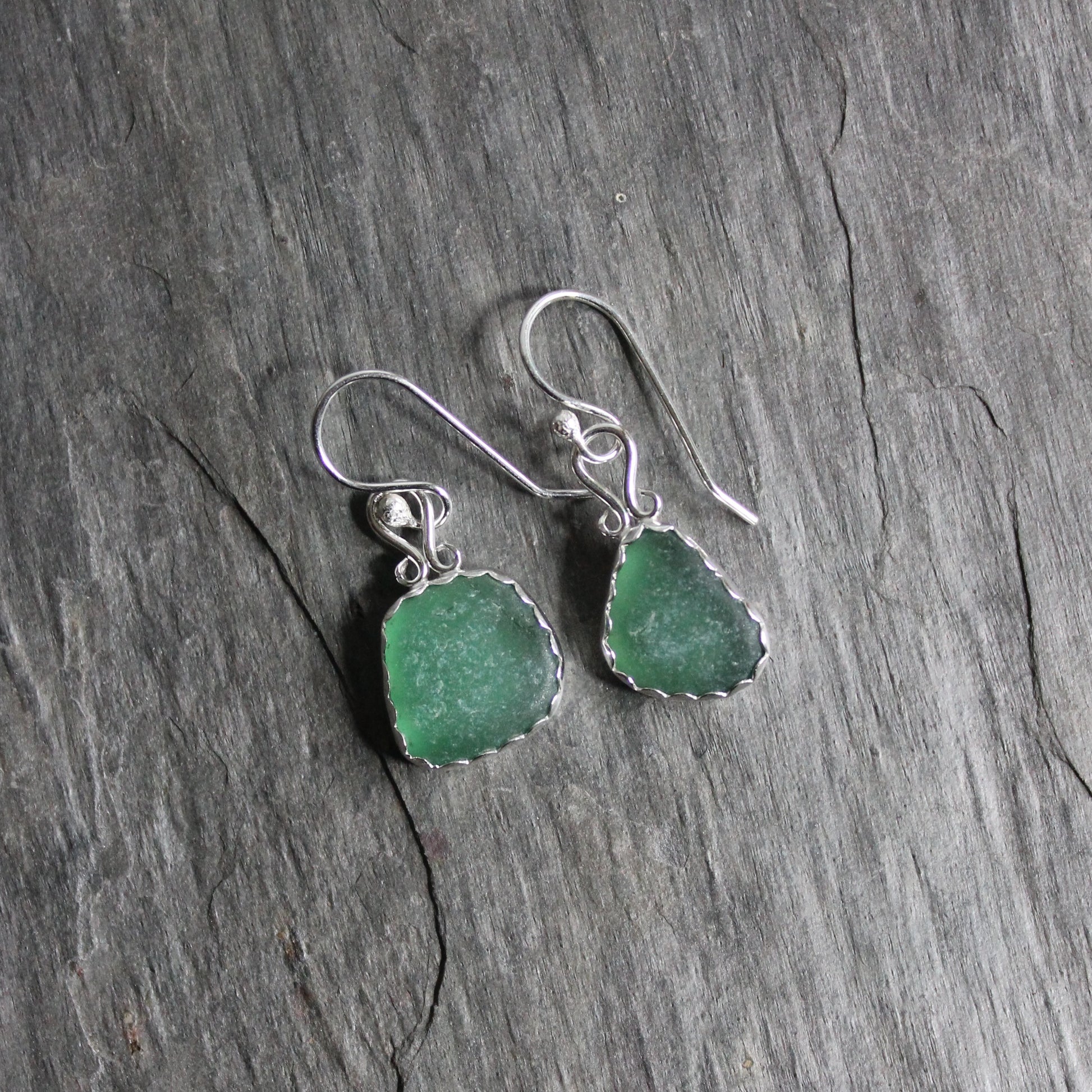 Dark green dangly sea glass earrings made with a sterling and fine silver scalloped bezel setting and a fancy bail on sterling silver ear wires. 