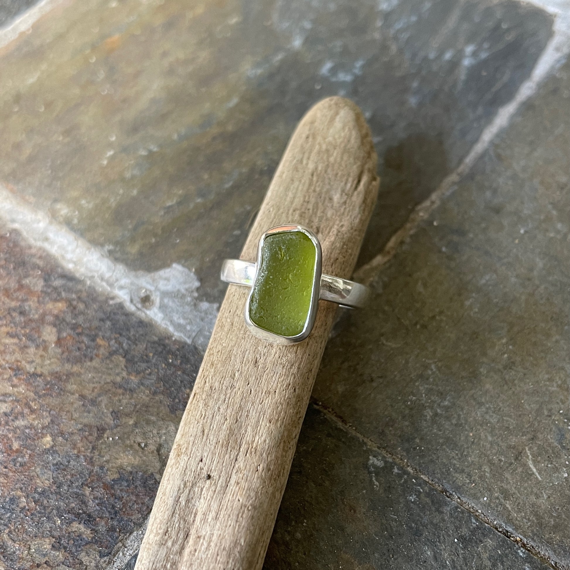 This is a small oblong piece of olive green sea glass set in a fine & sterling silver bezel setting on a sturdy hammered band.  Size 6 1/2