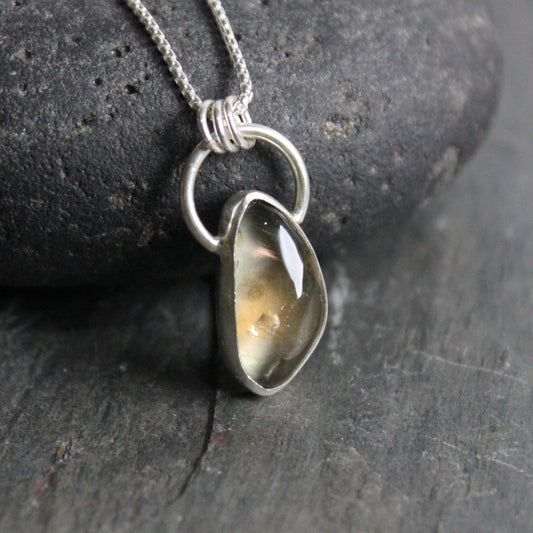 This is a small freeform Oregon sunstone with hints of green and peach.  It is set in a fine & sterling silver bezel setting and comes on an 18" chain. 