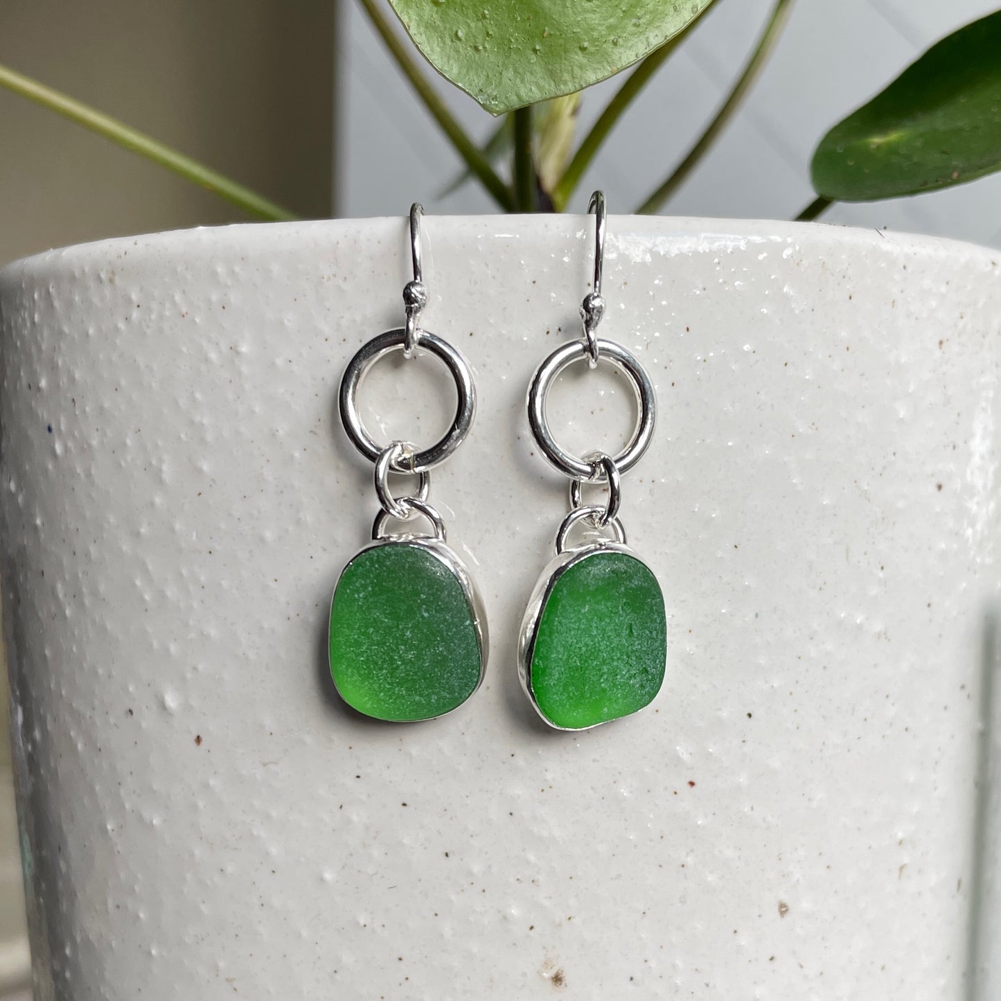This is a pair of dangly bright green sea glass earrings with approximately 1/2" sea glass set in fine and sterling silver bezel settings and attached to a ring & ear wires. Accent Yourself specializes in sterling silver jewelry handmade by Barb Macy and Will Macy in Corvallis, OR including sea glass jewelry, Oregon sunstones, sterling silver earrings, and jewelry made with gemstones found in the Pacific Northwest.