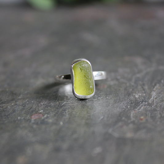 This is a small oblong piece of olive green sea glass set in a fine & sterling silver bezel setting on a sturdy hammered band.  Size 6 1/2