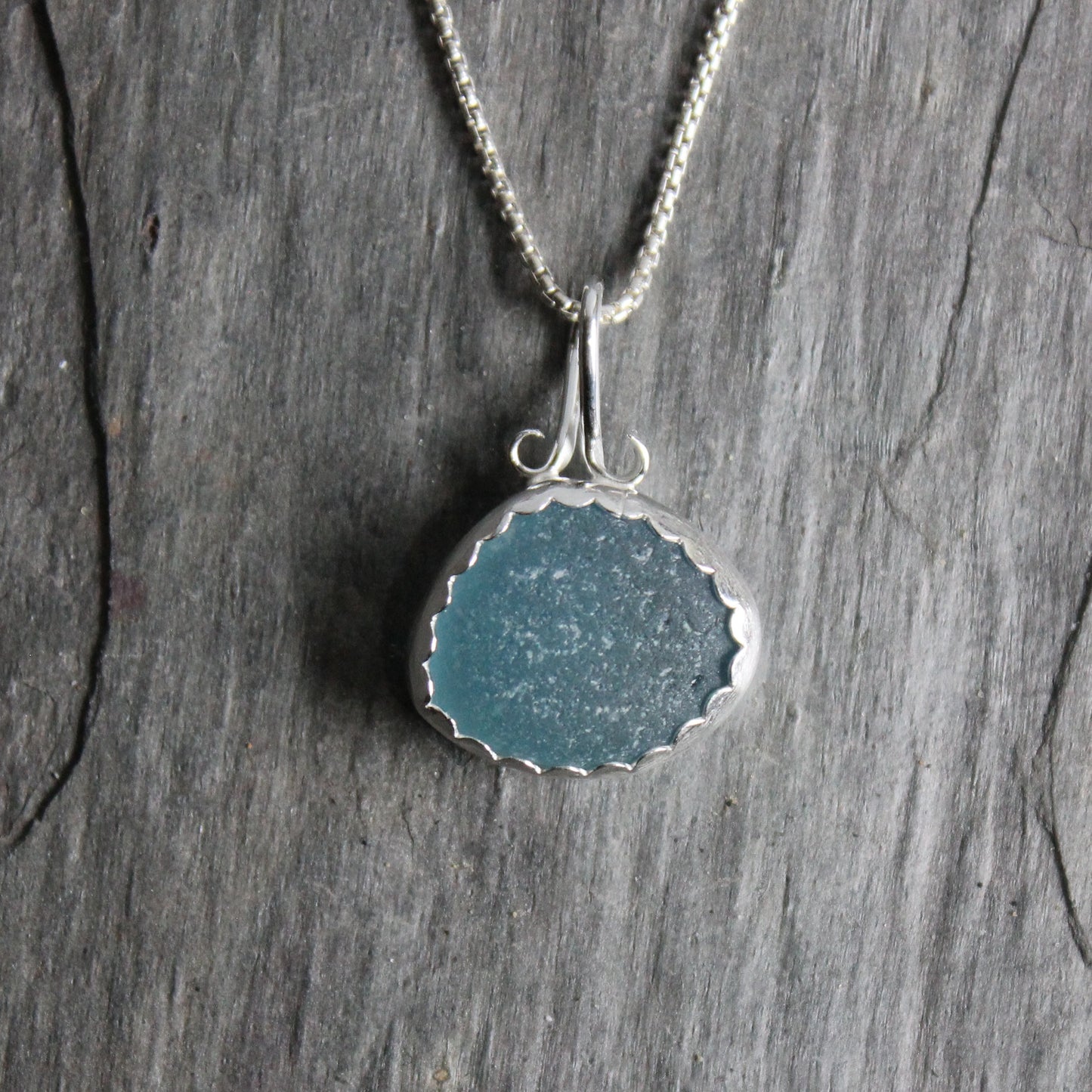 This is a large piece of teal sea glass set in a fine and sterling silver scalloped bezel setting with a fancy bail. 