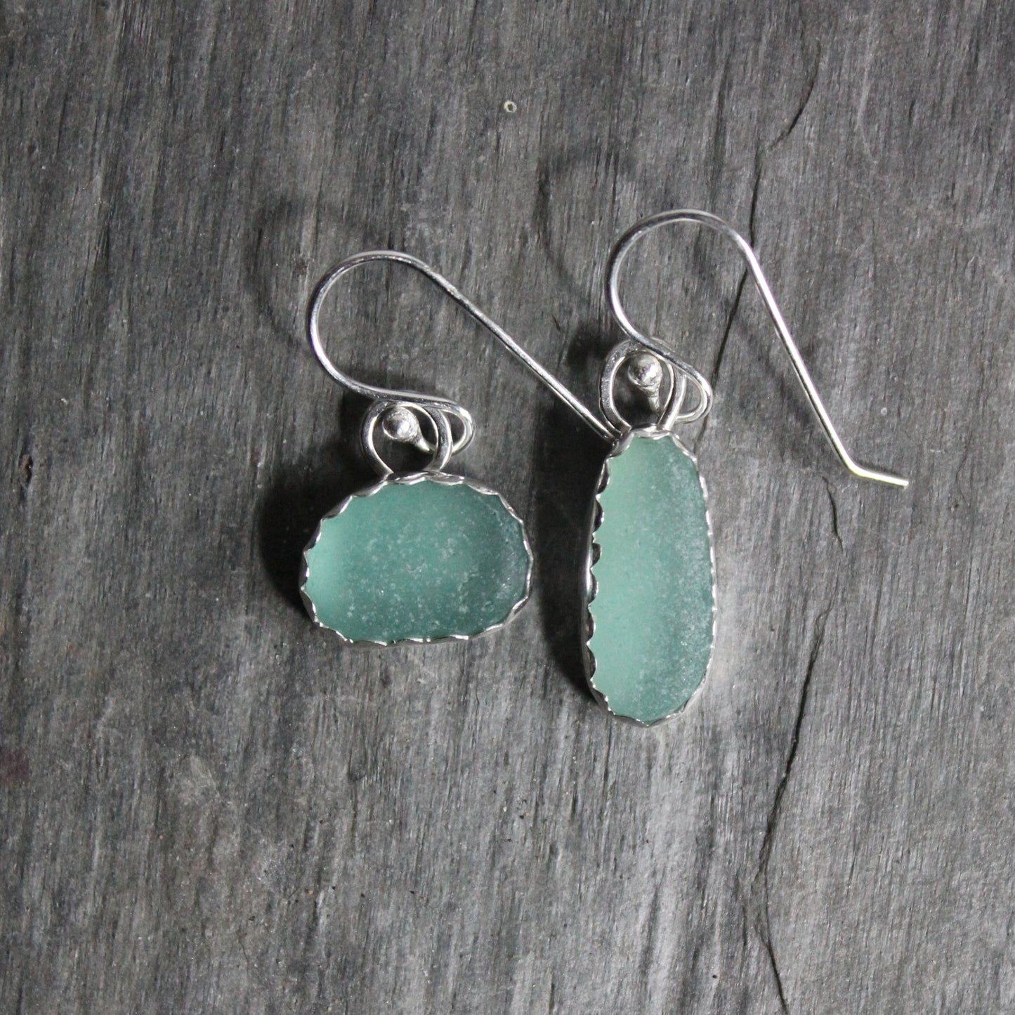 A mismatched pair of teal sea glass set in a scalloped fine and sterling silver bezel setting on handmade sterling ear wires. 