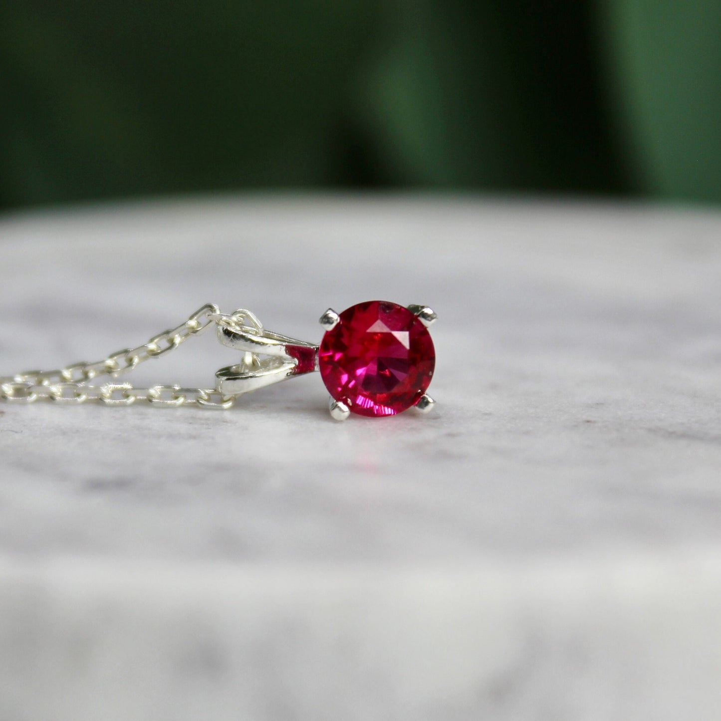 This necklace has a 6mm round simulated ruby set in a sterling silver 4-prong pendant setting on a sterling silver chain.