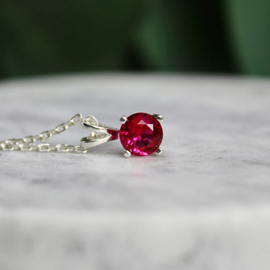 This necklace has a 6mm round simulated ruby set in a sterling silver 4-prong pendant setting on a sterling silver chain.