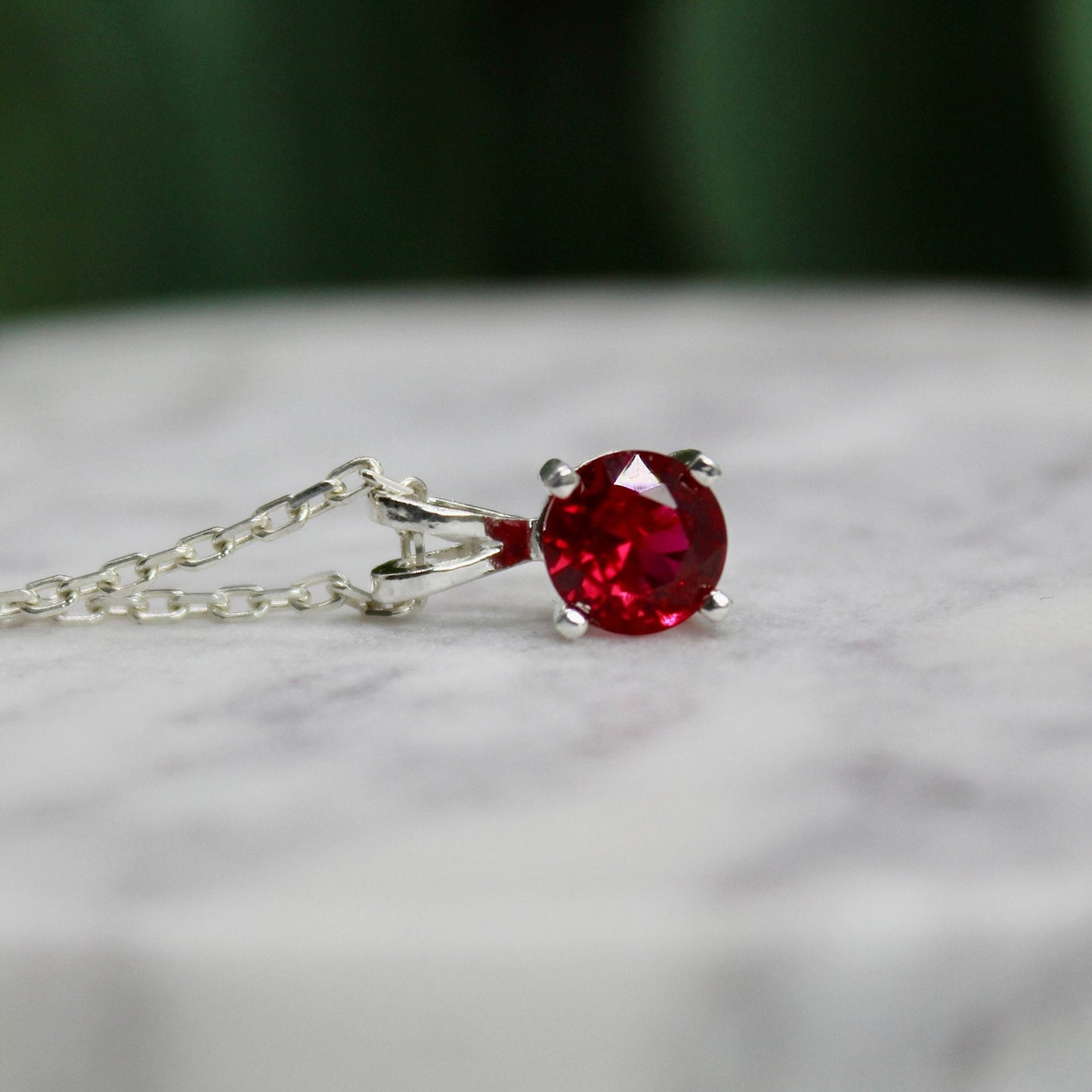 This necklace has a 6mm round faceted lab created garnet set in a sterling silver 4-prong pendant setting on a sterling silver chain.