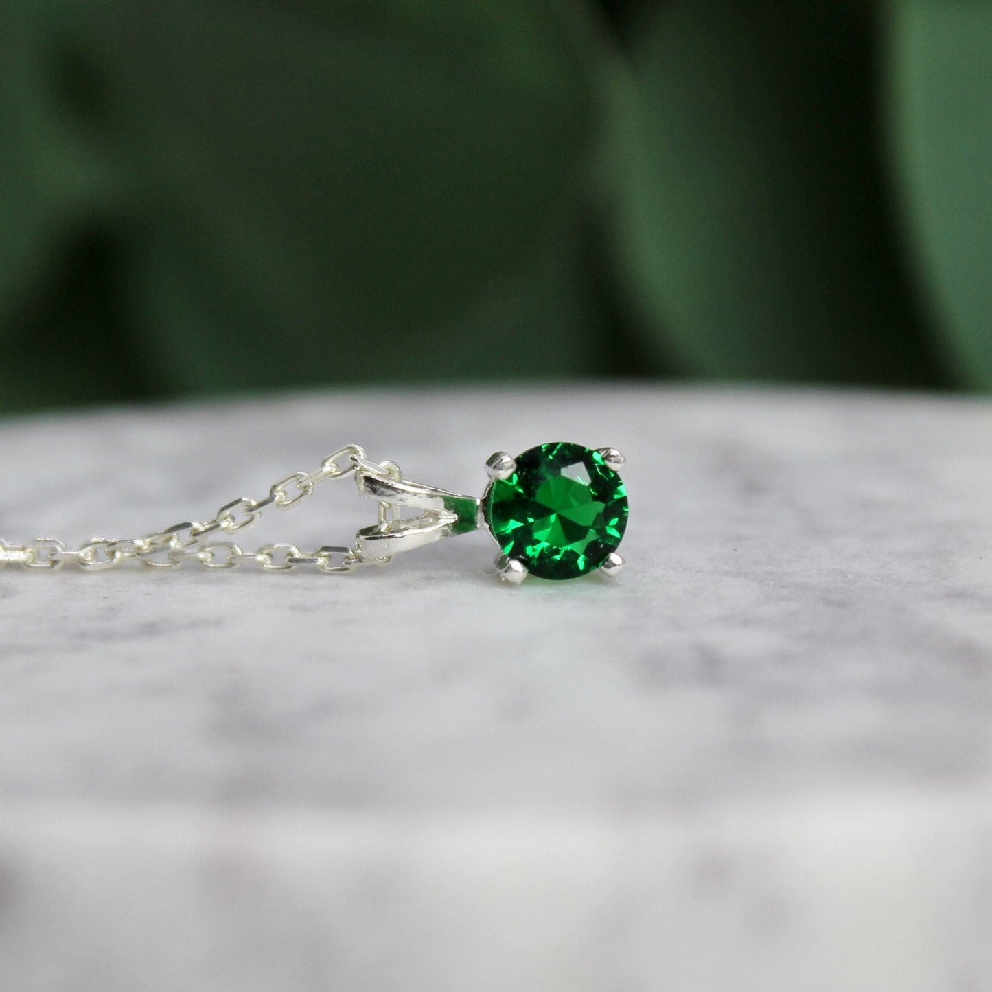 This necklace has a 6mm round faceted lab created emerald set in a sterling silver 4-prong pendant setting on a sterling silver chain.