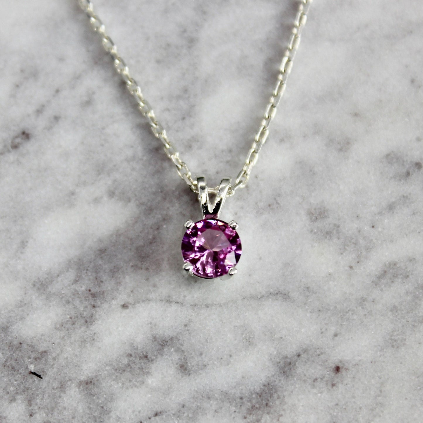 A 6mm round simulated pink tourmaline faceted gemstone set in a 4-prong sterling silver pendant setting on a sterling silver chain.