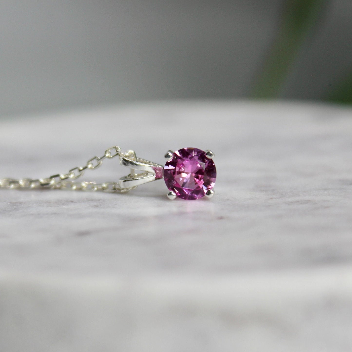 This necklace has a 6mm round faceted lab created pink tourmaline gemstone set in a sterling silver 4-prong setting on a sterling silver chain.