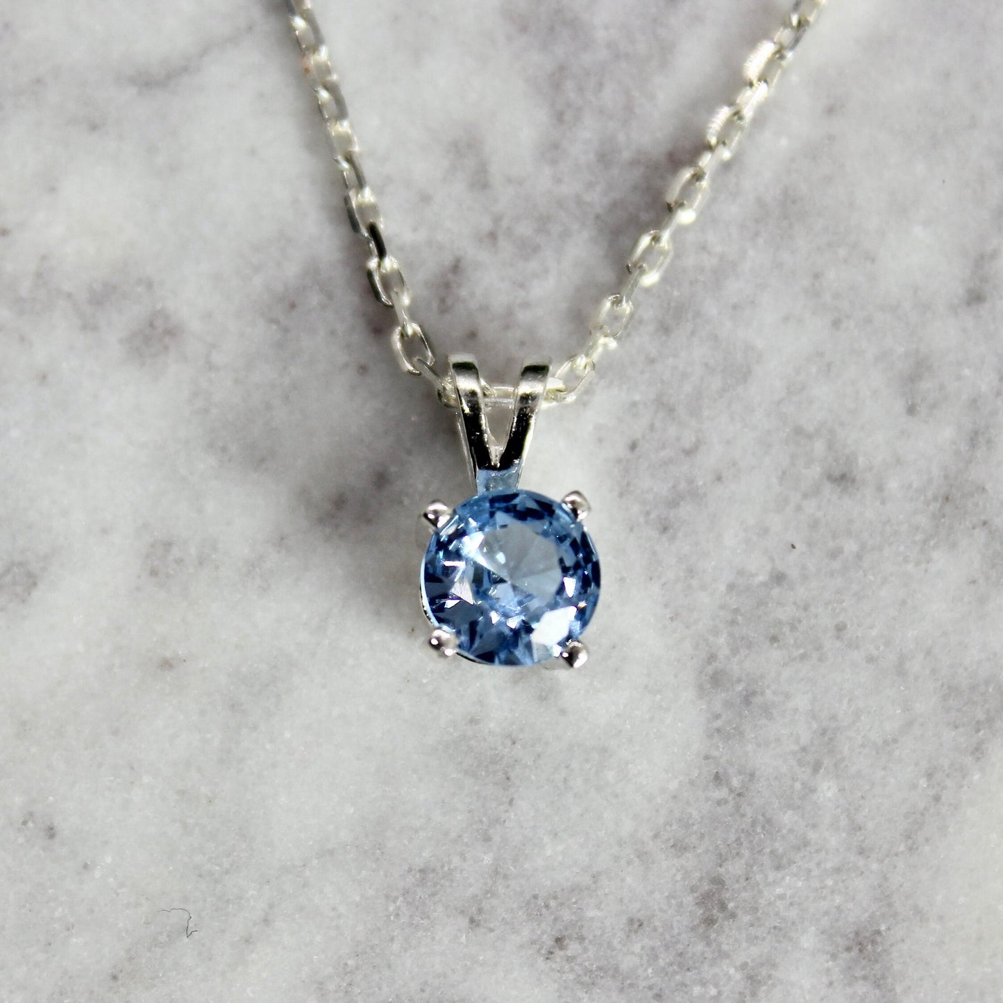 This necklace has a 6mm round faceted lab created aquamarine set in a sterling silver 4-prong pendant setting on a sterling silver chain.