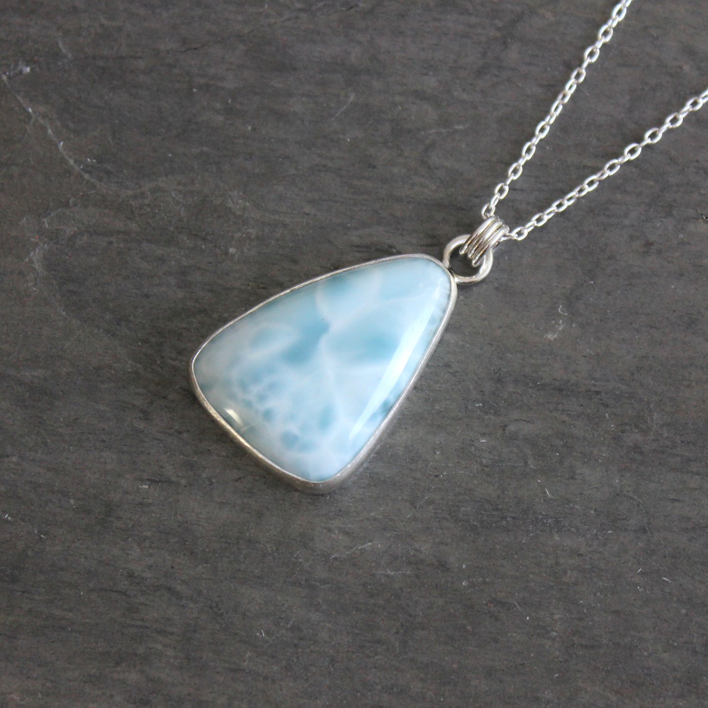Necklace with a triangular blue larimar pendant on a dark gray background