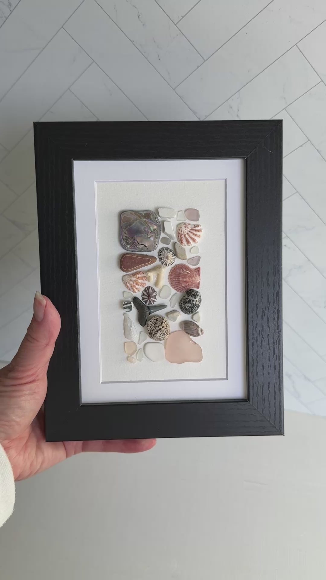 Framed artwork with sea glass and shells on a white background