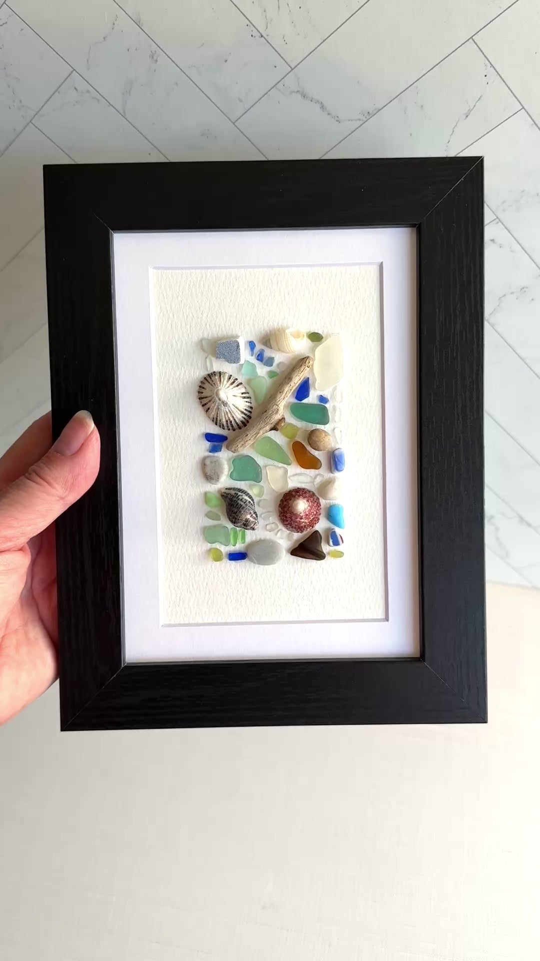 Framed artwork with seashells and sea glass pieces on a white background