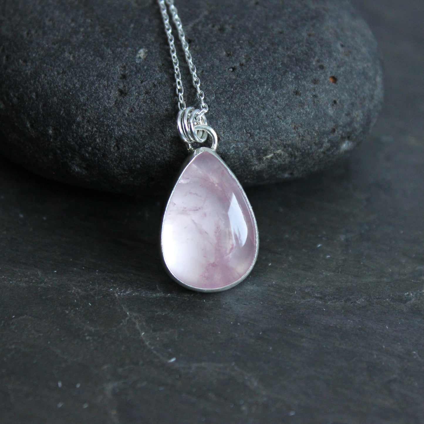 Teardrop-shaped pink pendant on a silver chain against a dark stone background
