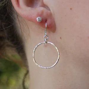 A model wearing 1 inch hammered dangly circle earrings made with sterling silver and hangs about 1.5" from the ear. 