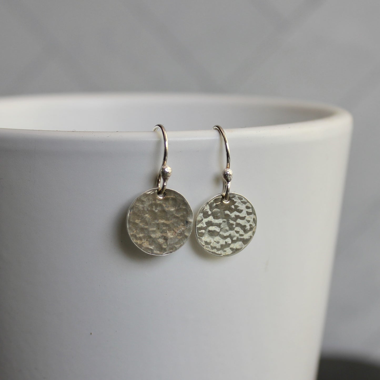 Silver round earrings on a white cup with a gray background