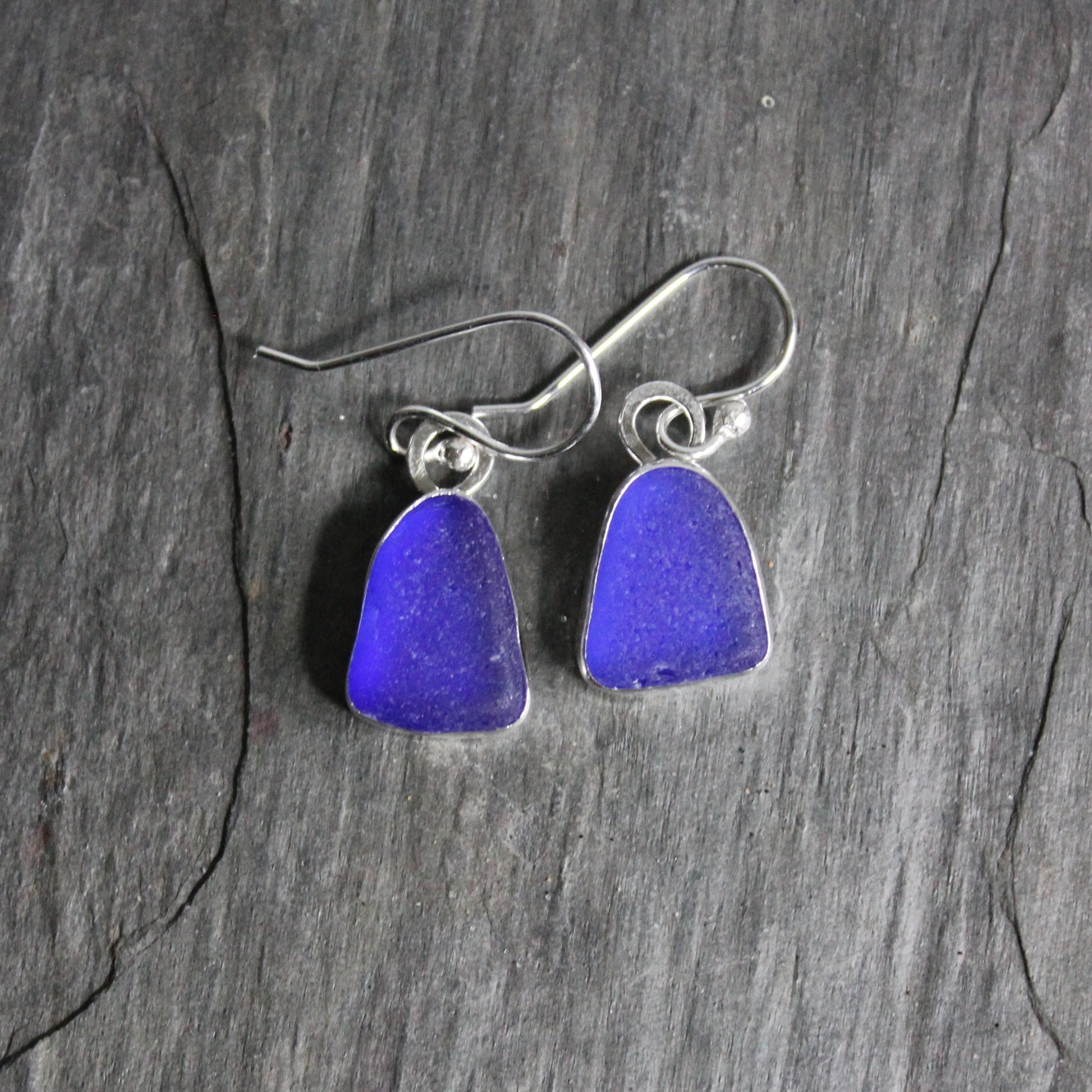 These are small dangly cobalt blue sea glass earrings that are set in a fine and sterling silver bezel setting on silver ear wires. 