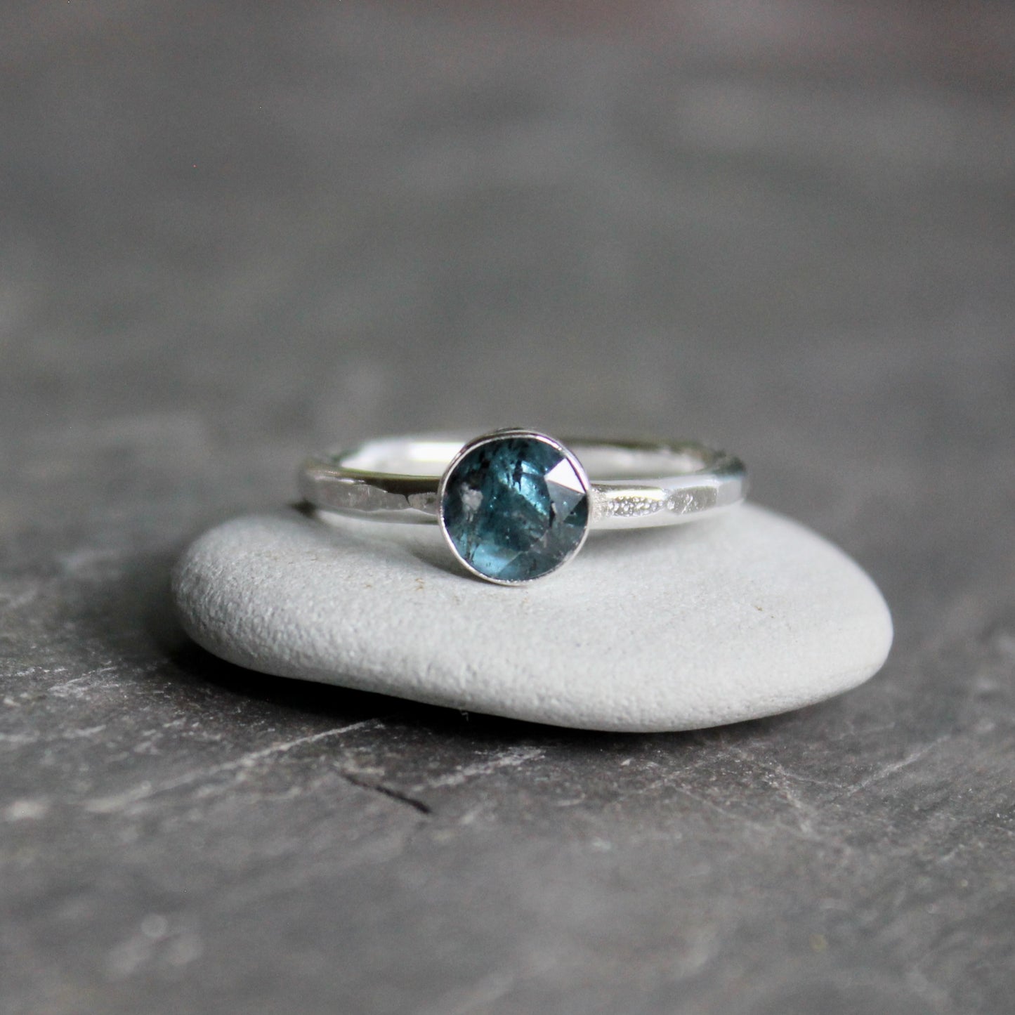 Silver ring with a teal kyanite gemstone on a gray surface