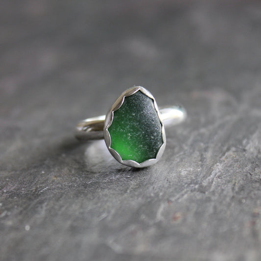 This is a small chunky piece of dark green sea glass set in a fine and sterling silver scalloped bezel setting on a sturdy silver band.  Size 9