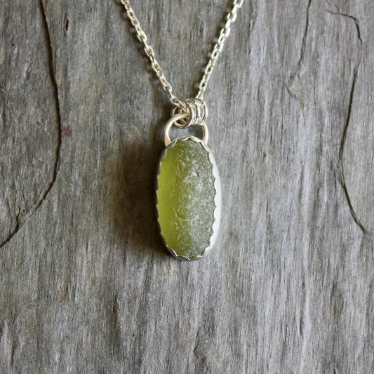 This is a long oval piece of olive green sea glass set in a fine and sterling silver scalloped bezel setting with an 18" chain. 