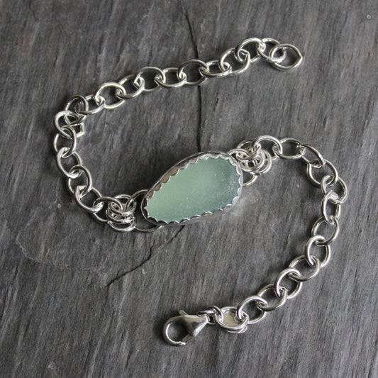 This bracelet has a light sage green piece of sea glass set in a fine & sterling silver scalloped bezel finished with a heavy chain and lobster clasp. 