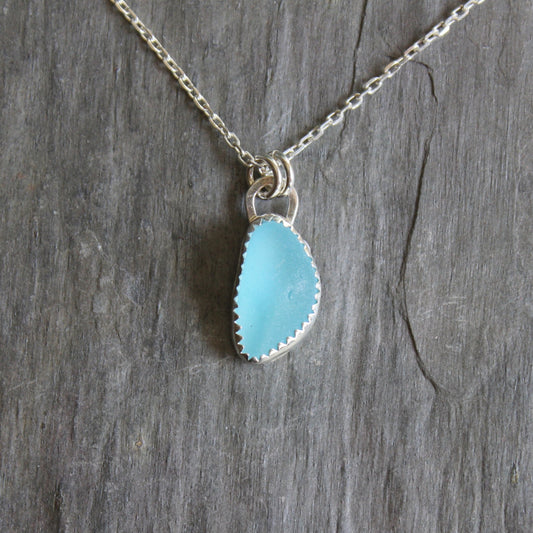 Small turquoise blue sea glass pendant set in fine and sterling silver serrated bezel setting on a silver chain. 