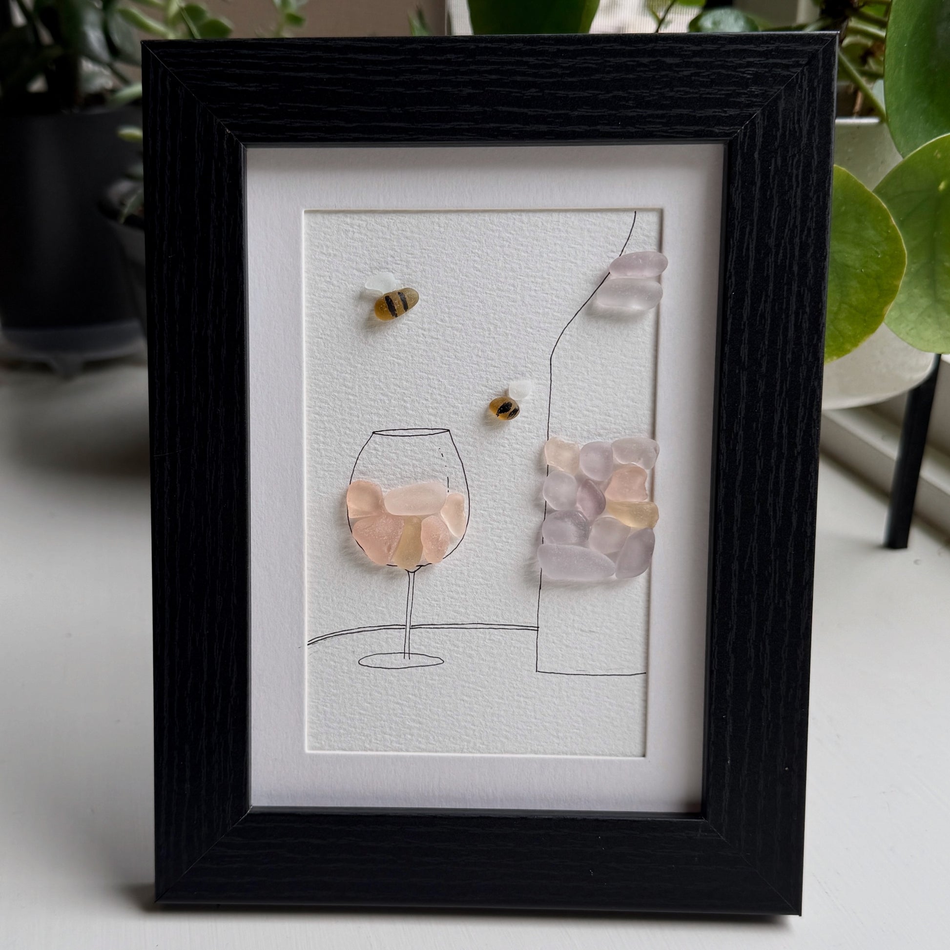 Framed artwork of a wine bottle and glass with decorative elements on a light background.