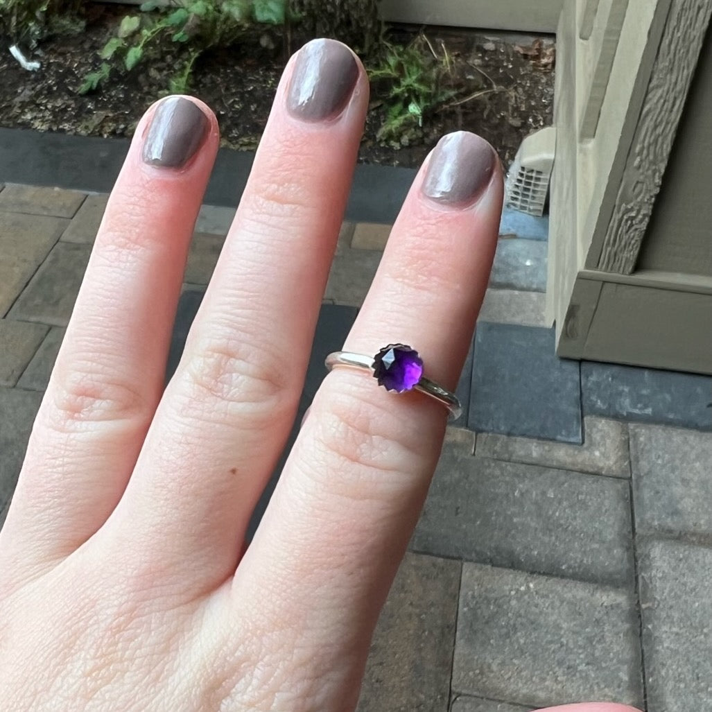 This is a 6mm rose cut round amethyst cabochon set in a sterling silver bezel setting on a sturdy silver band modeled on a hand.