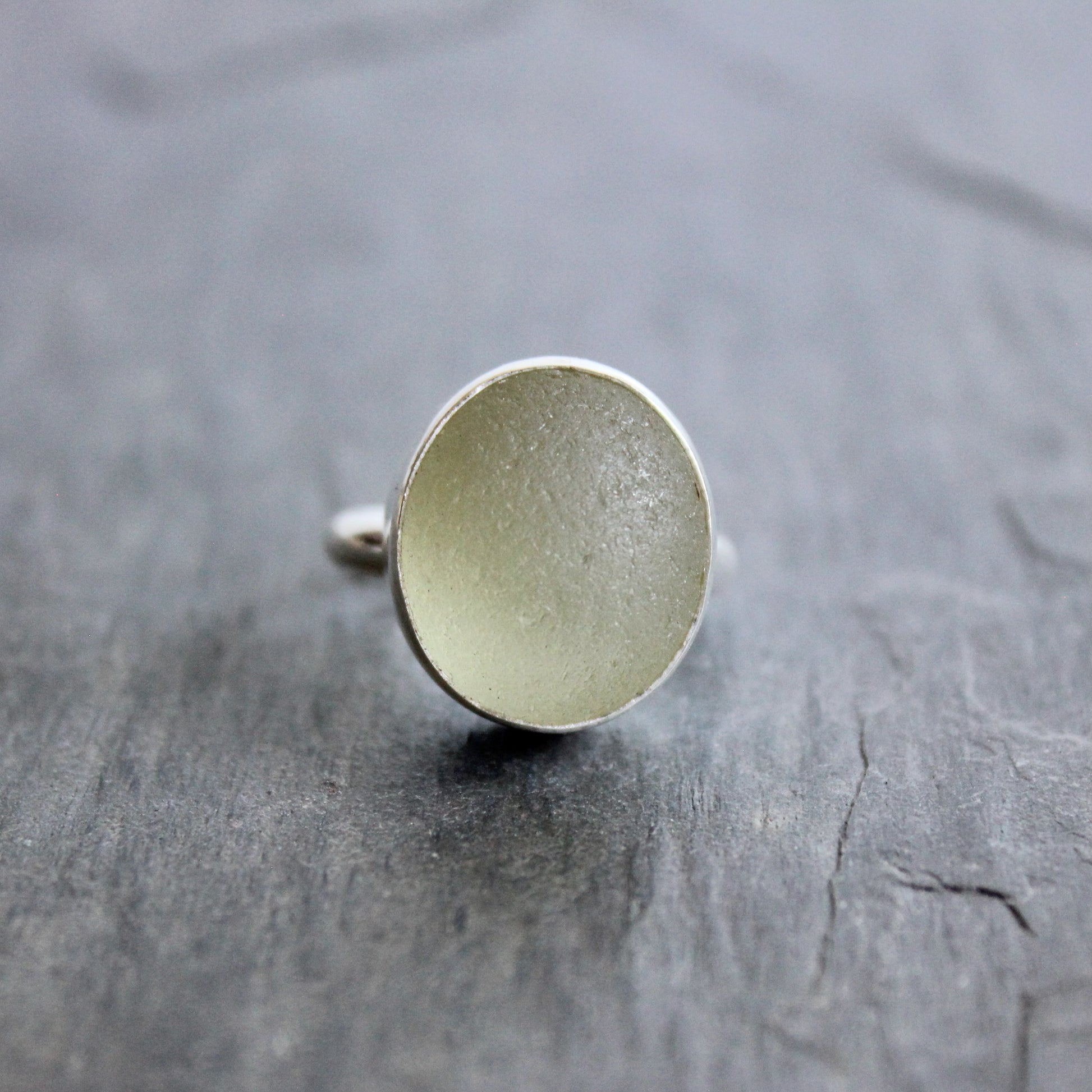 Silver ring with a Champagne Sea Glass setting on a grey surface