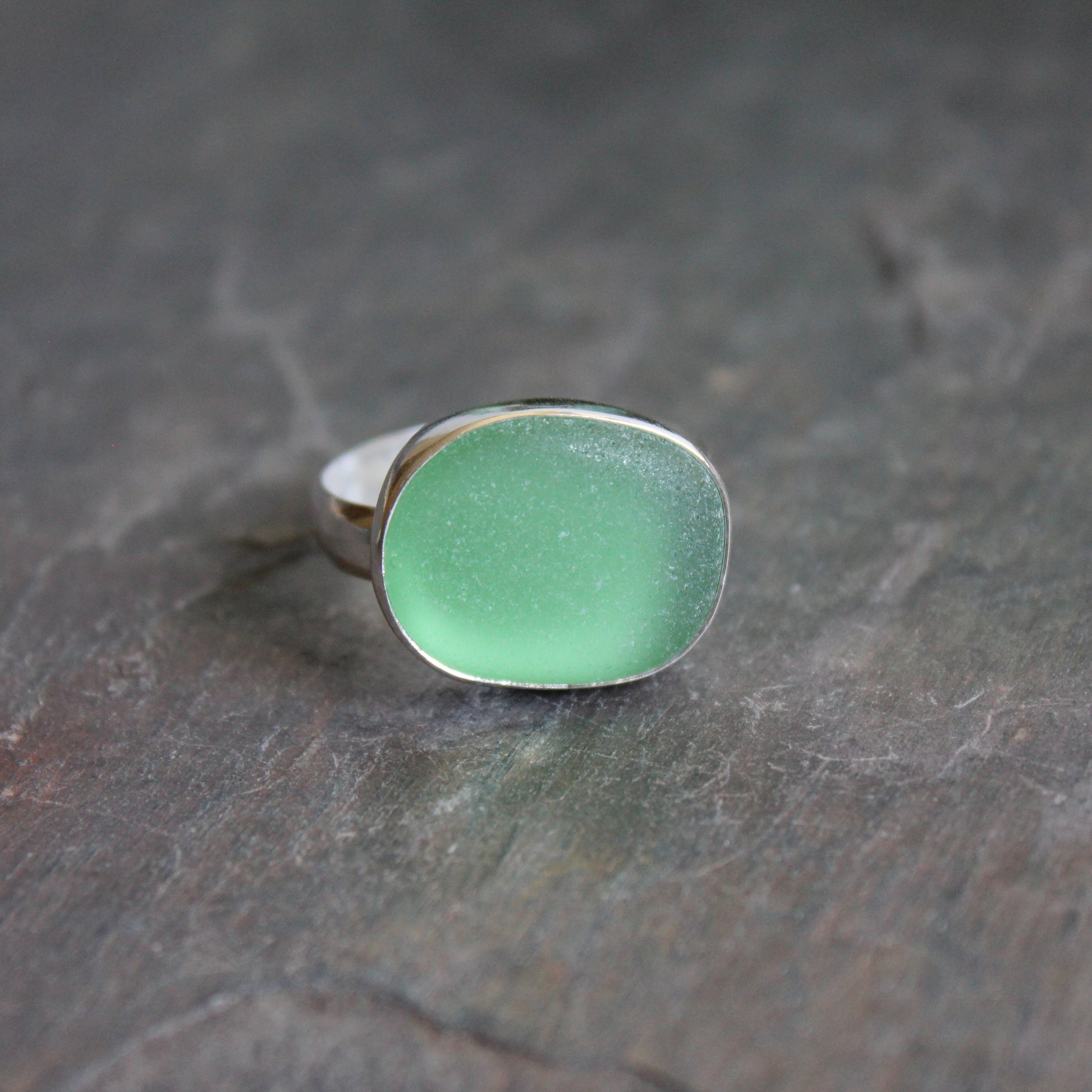 Huge green sea glass ring with silver band on a textured dark surface.