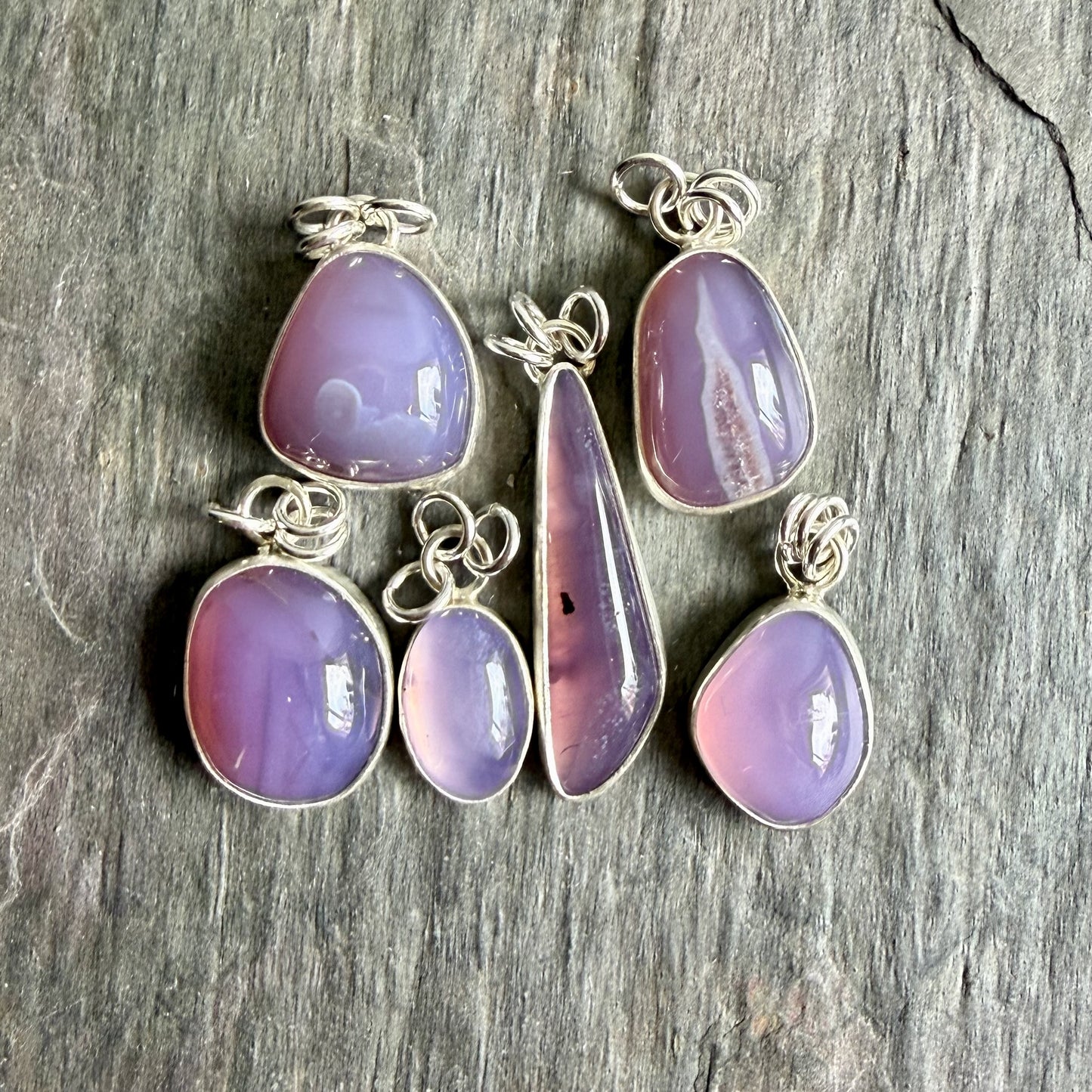 Set of purple teardrop pendants on silver chains against a wooden background