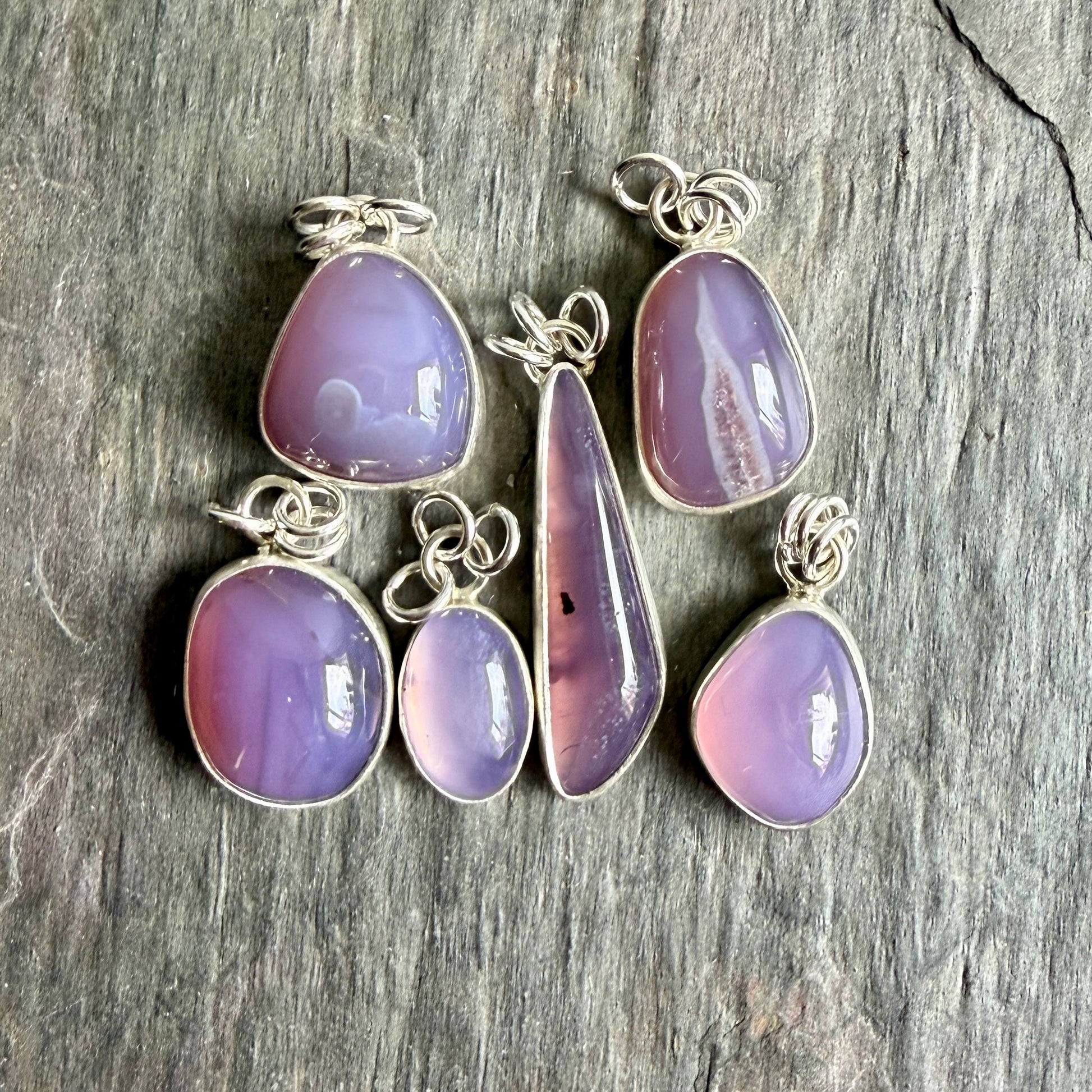 Set of purple teardrop pendants on silver chains against a wooden background
