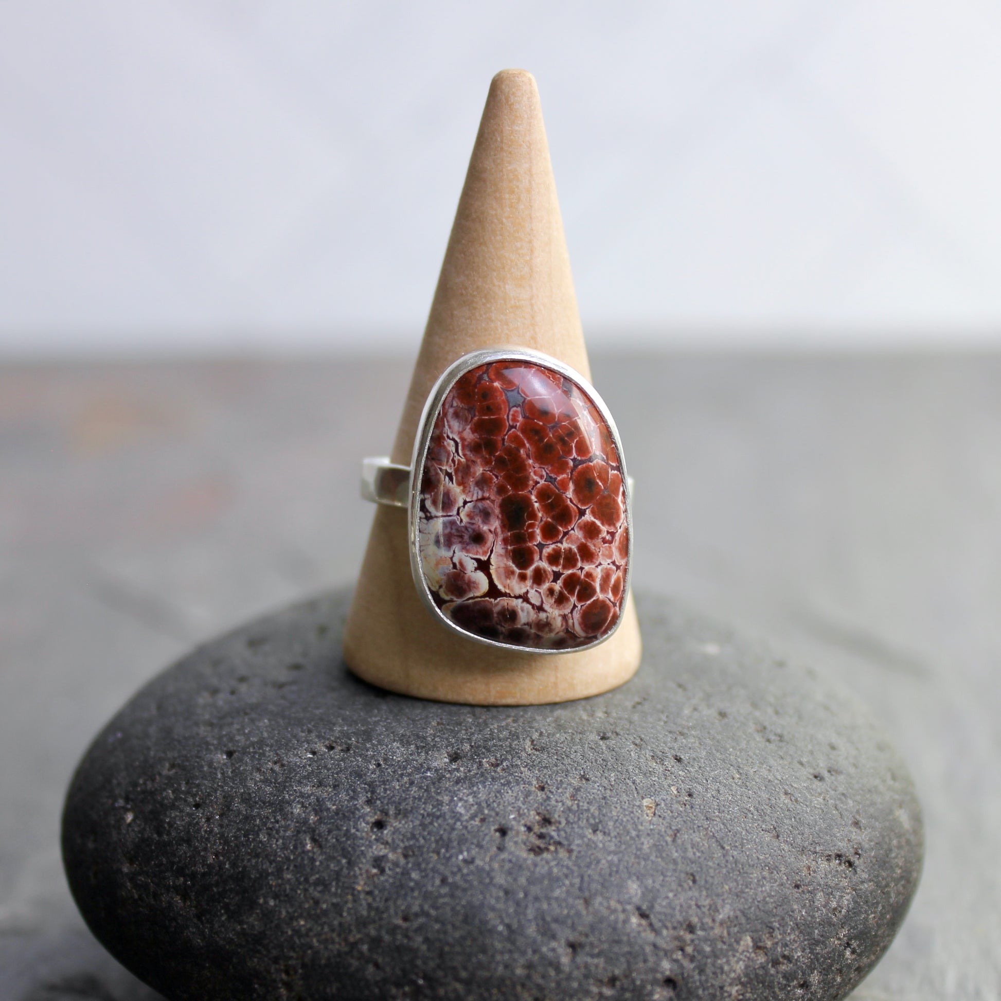 This pretty ring has a locally-sourced red Oregon orbicular jasper that is set in a fine and sterling silver bezel and on a sturdy silver hammered band. Handmade by Will Macy in Corvallis, OR.