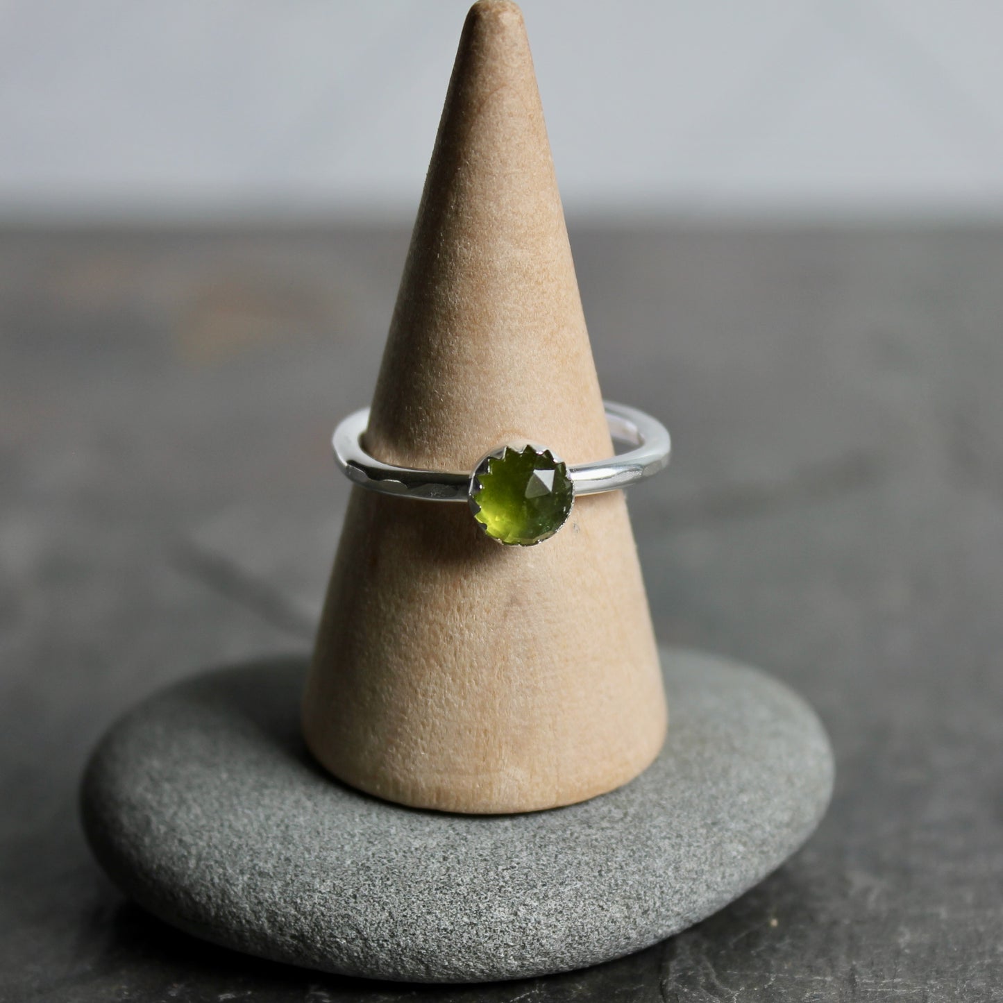 Silver ring with a green gemstone on a cone-shaped stand against a gray background