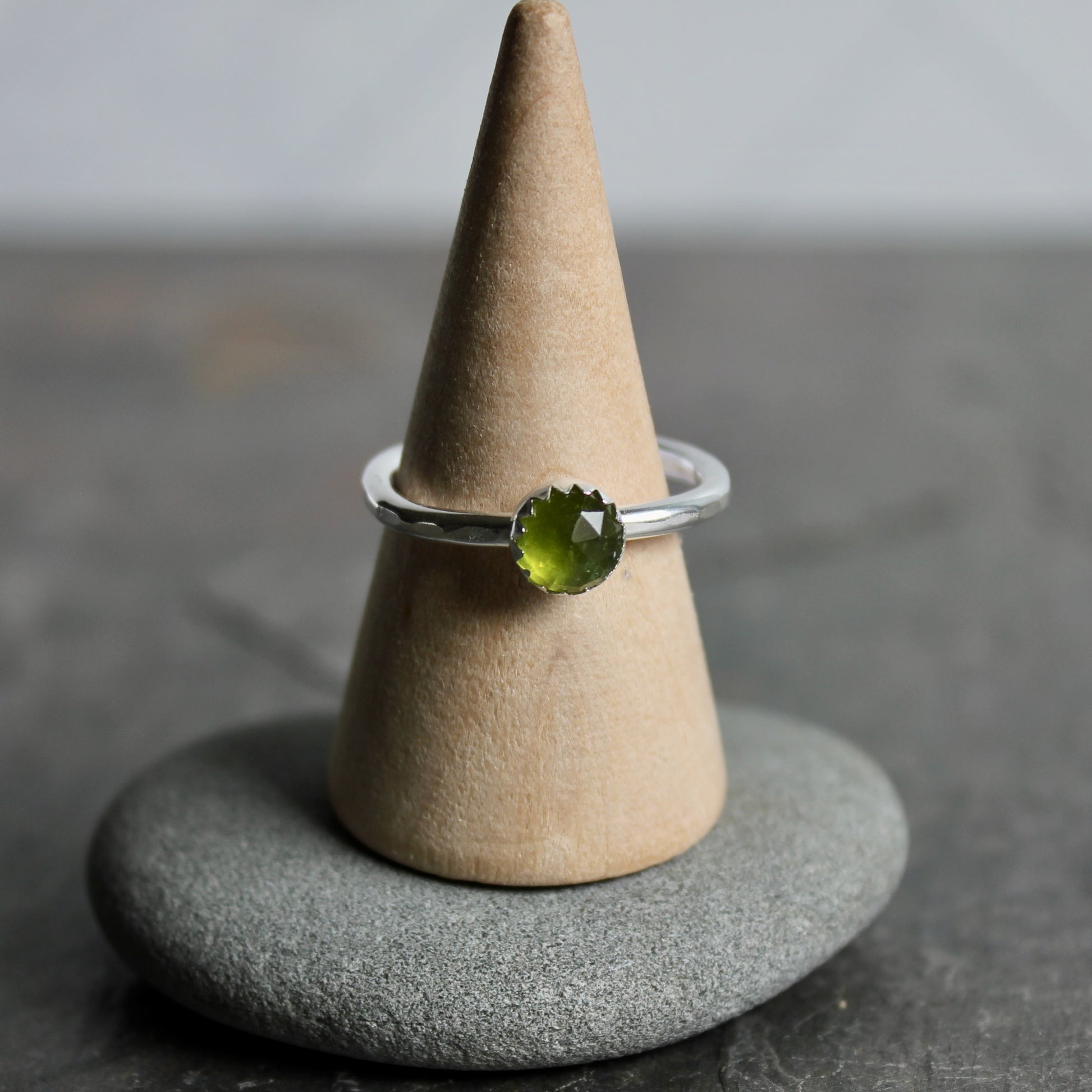 Silver ring with a green gemstone on a cone-shaped stand against a gray background